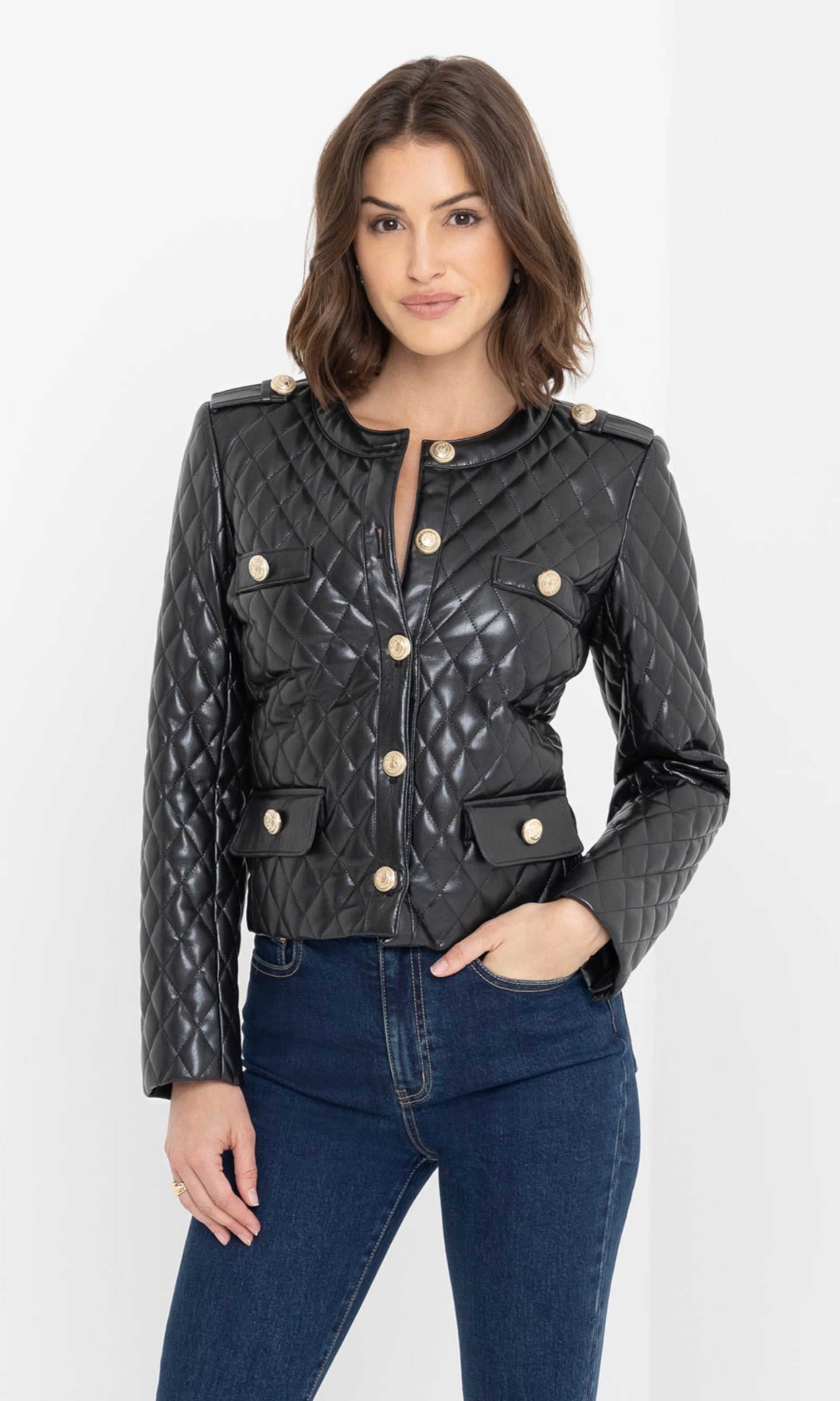 The model poses in a mid shot wearing the Brevel Quilted Vegan Leather Jacket in black, draping it open to reveal a lace cami underneath.
