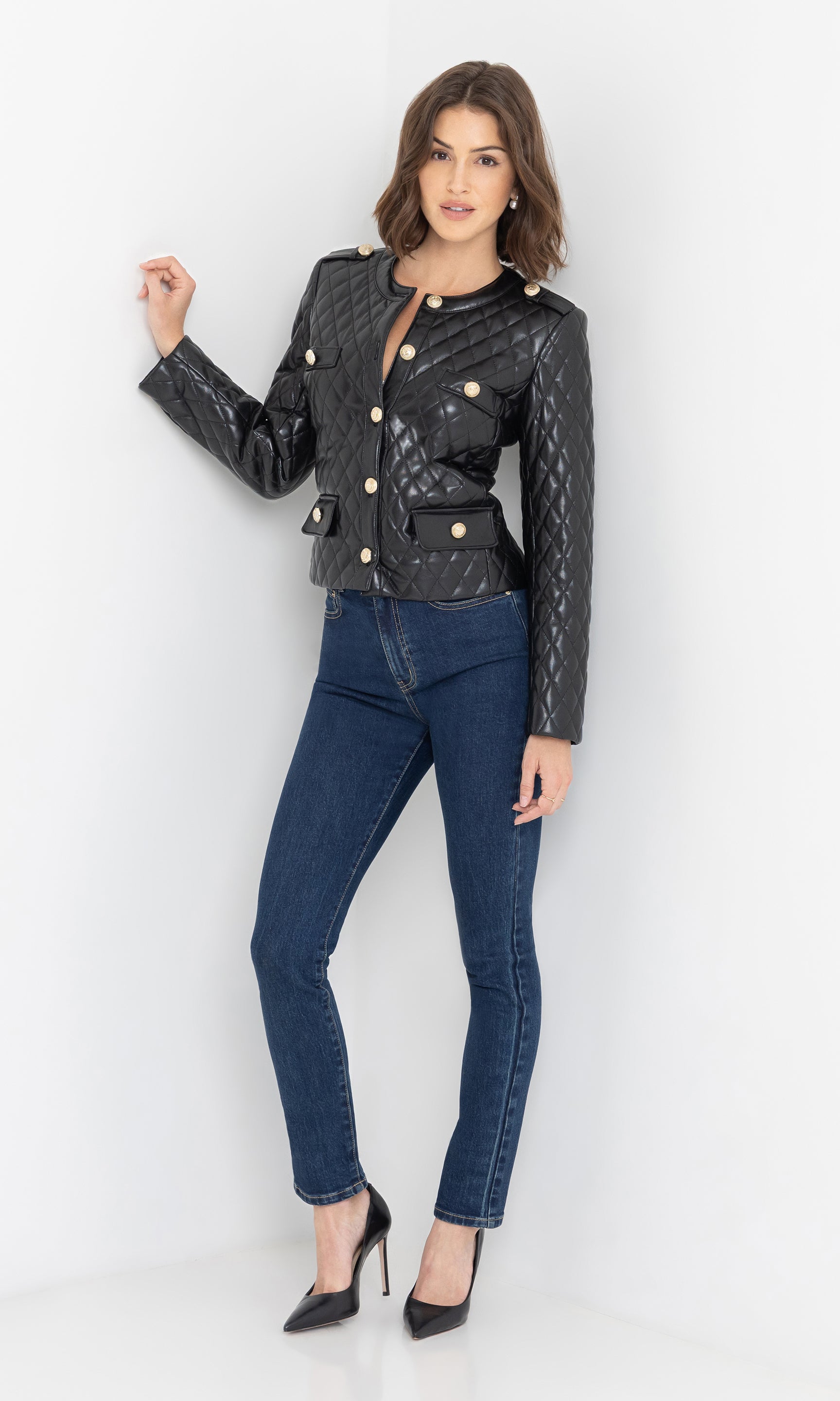 The model poses in a full body front view wearing the Brevel Quilted Vegan Leather Jacket in black against a white studio corner, highlighting its clean lines.