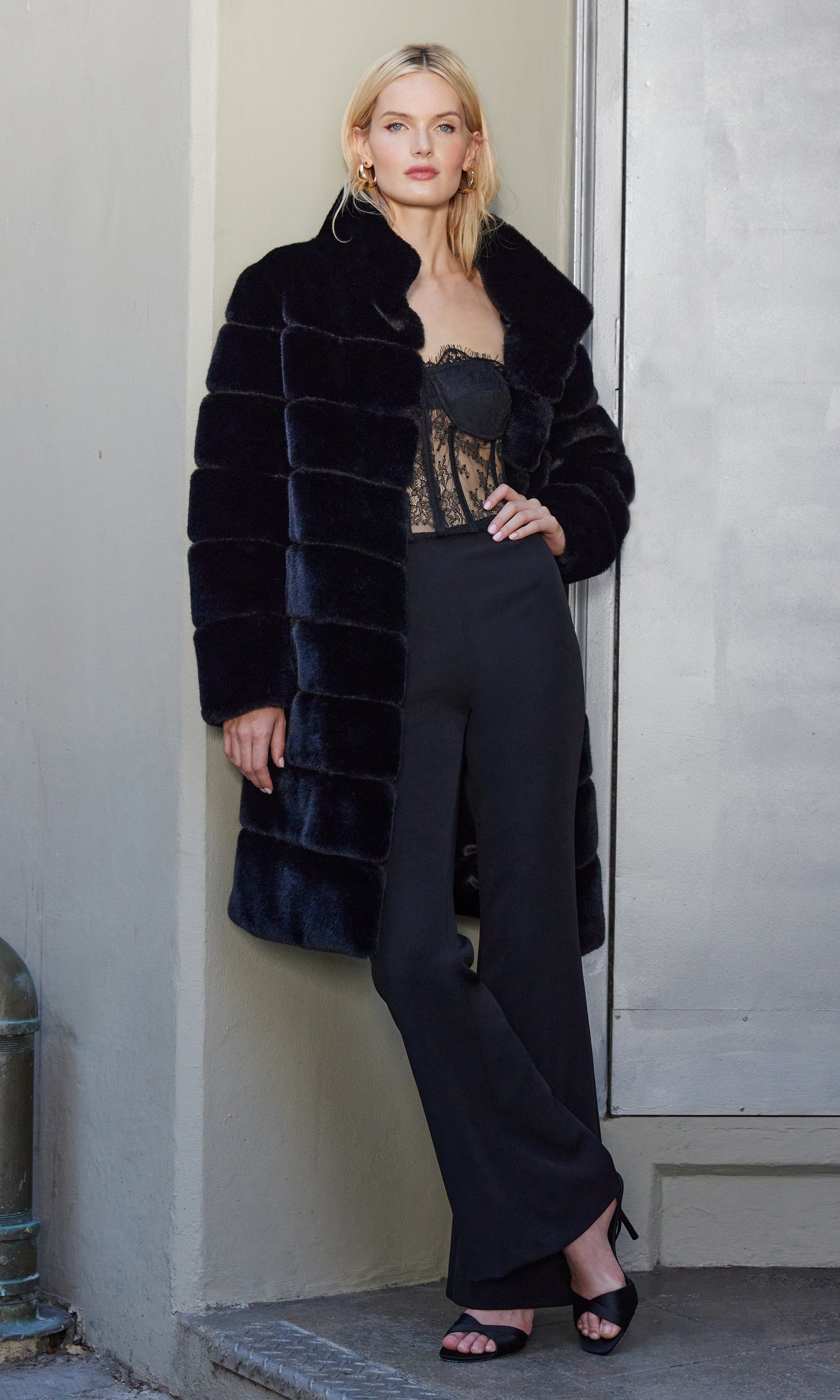 Woman wearing a black fur coat and black pants against a neutral background