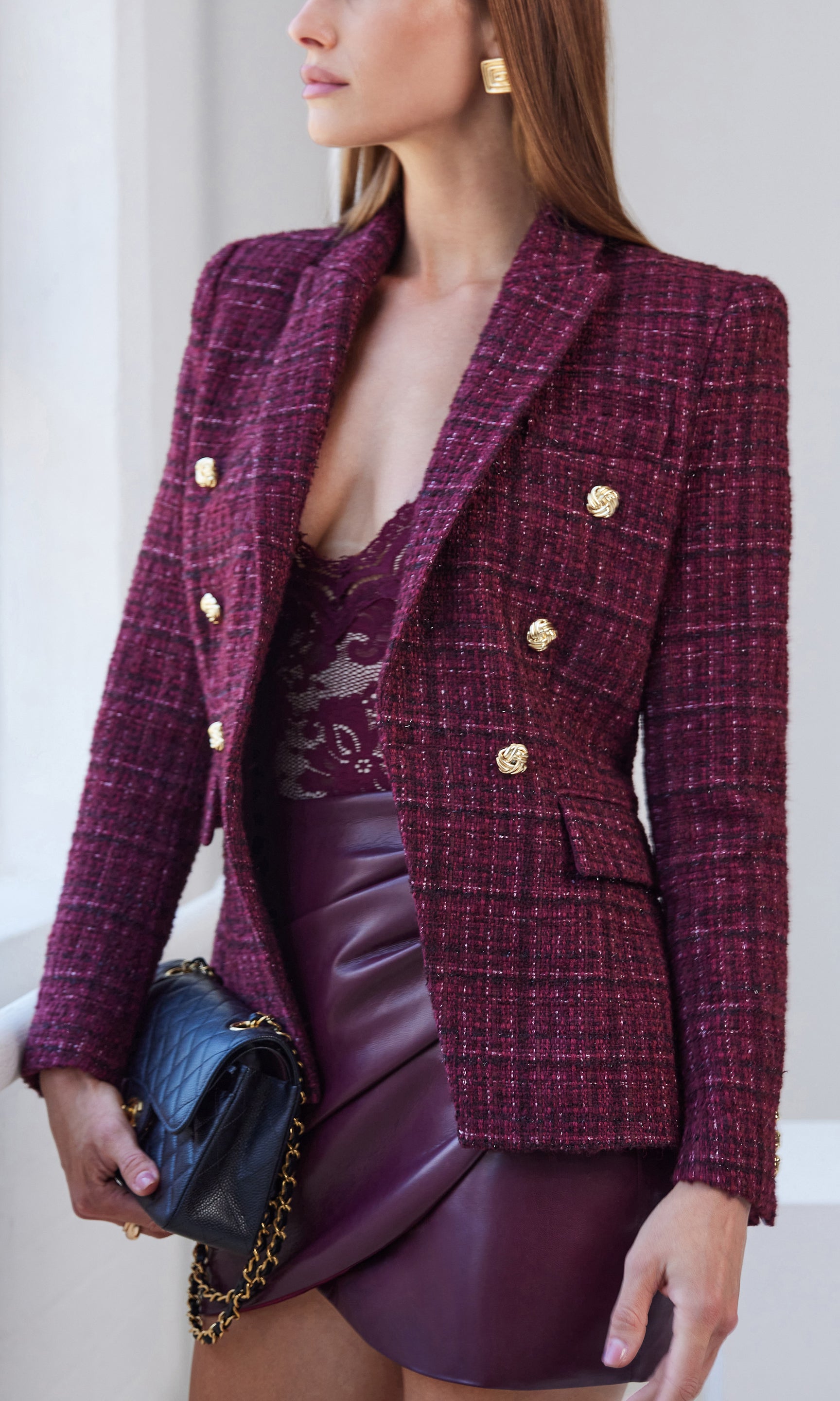 Woman wearing a burgundy tweed blazer with gold buttons, paired with a matching skirt.