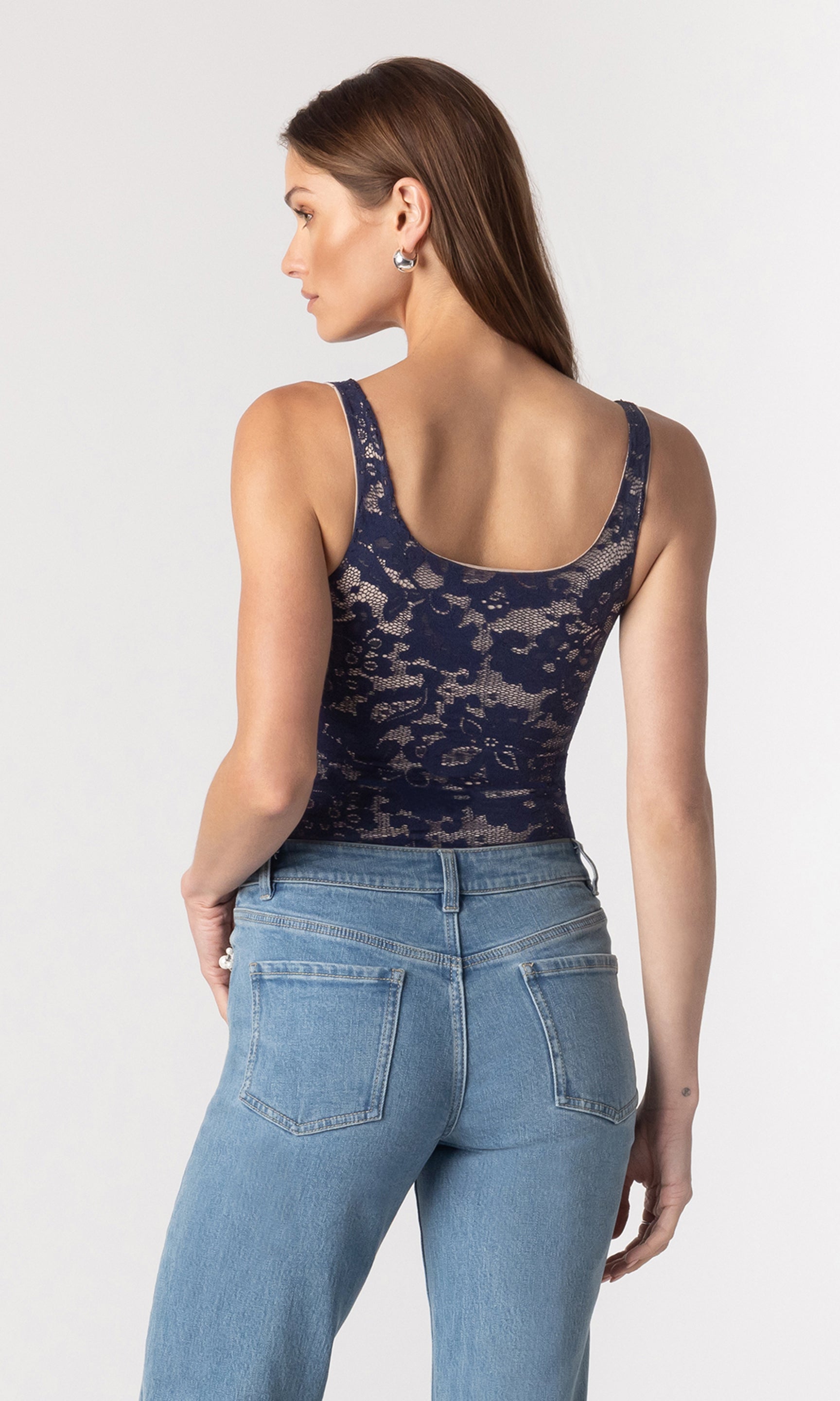 back image of model wearing the Gina lace bodysuit in a navy and beige color paired with blue jeans