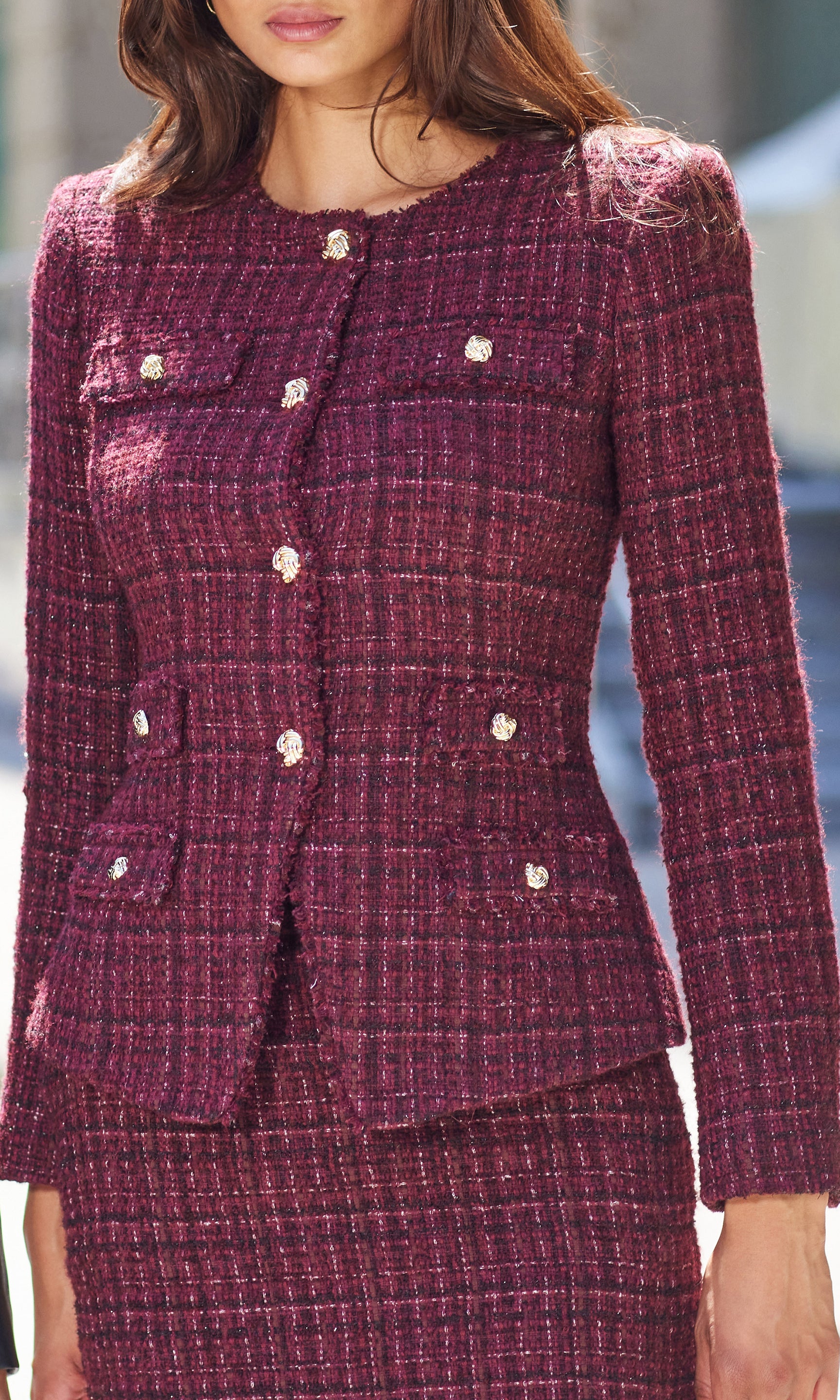 Close-up of a woman wearing a burgundy tweed suit with gold buttons.