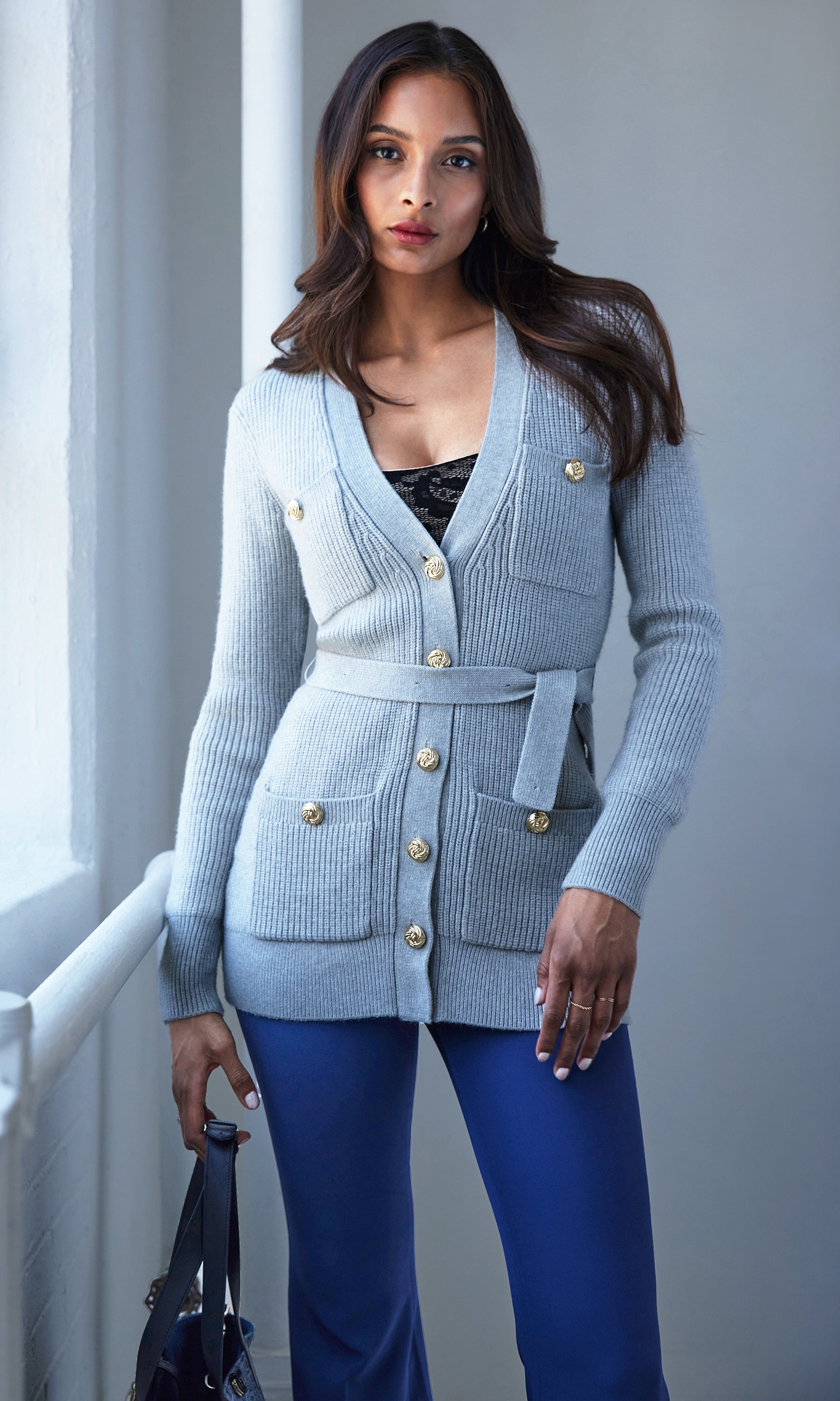 Woman wearing a grey cardigan with gold buttons in a neutral setting