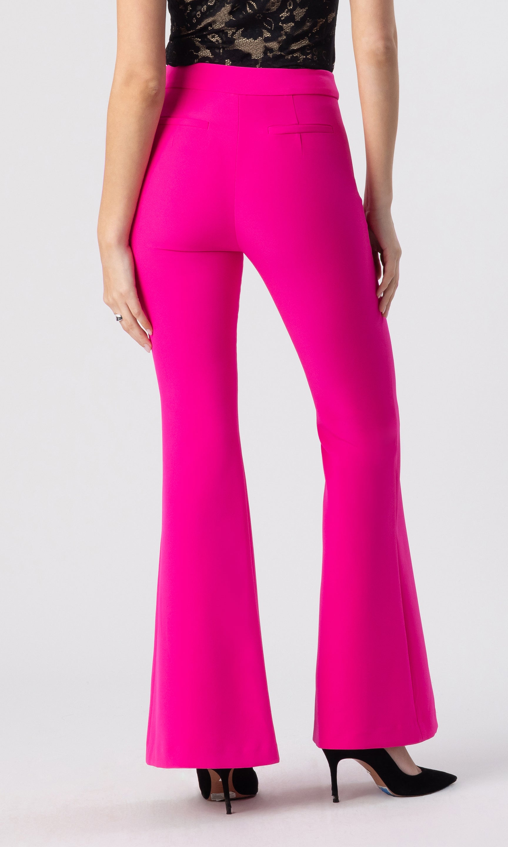 cropped back view image of model wearing the Wesley crepe pants in hot pink, paired with a black/beige lace top and black heels