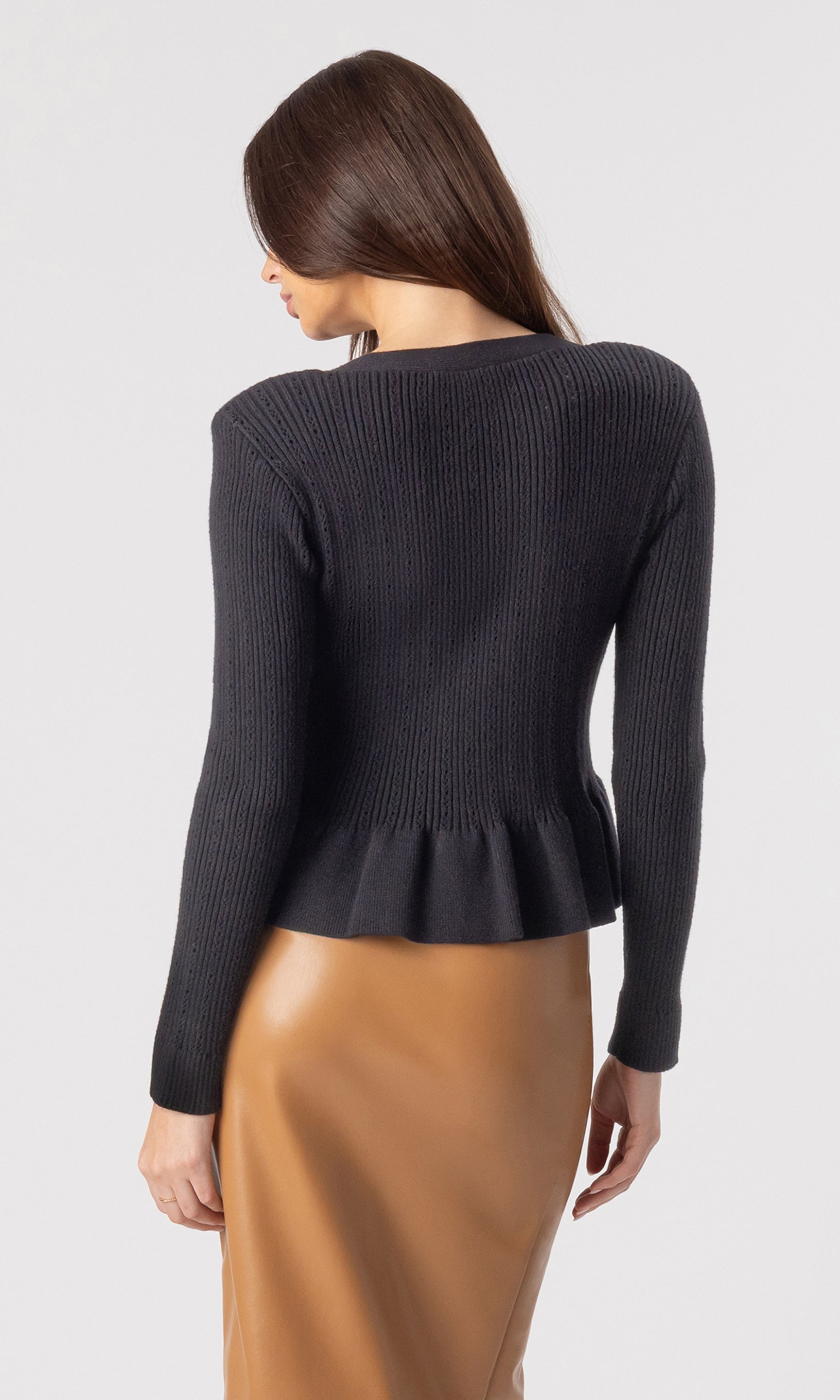 back view image of model wearing the Lirio Pointelle Cardigan in black paired with a brown vegan leather skirt