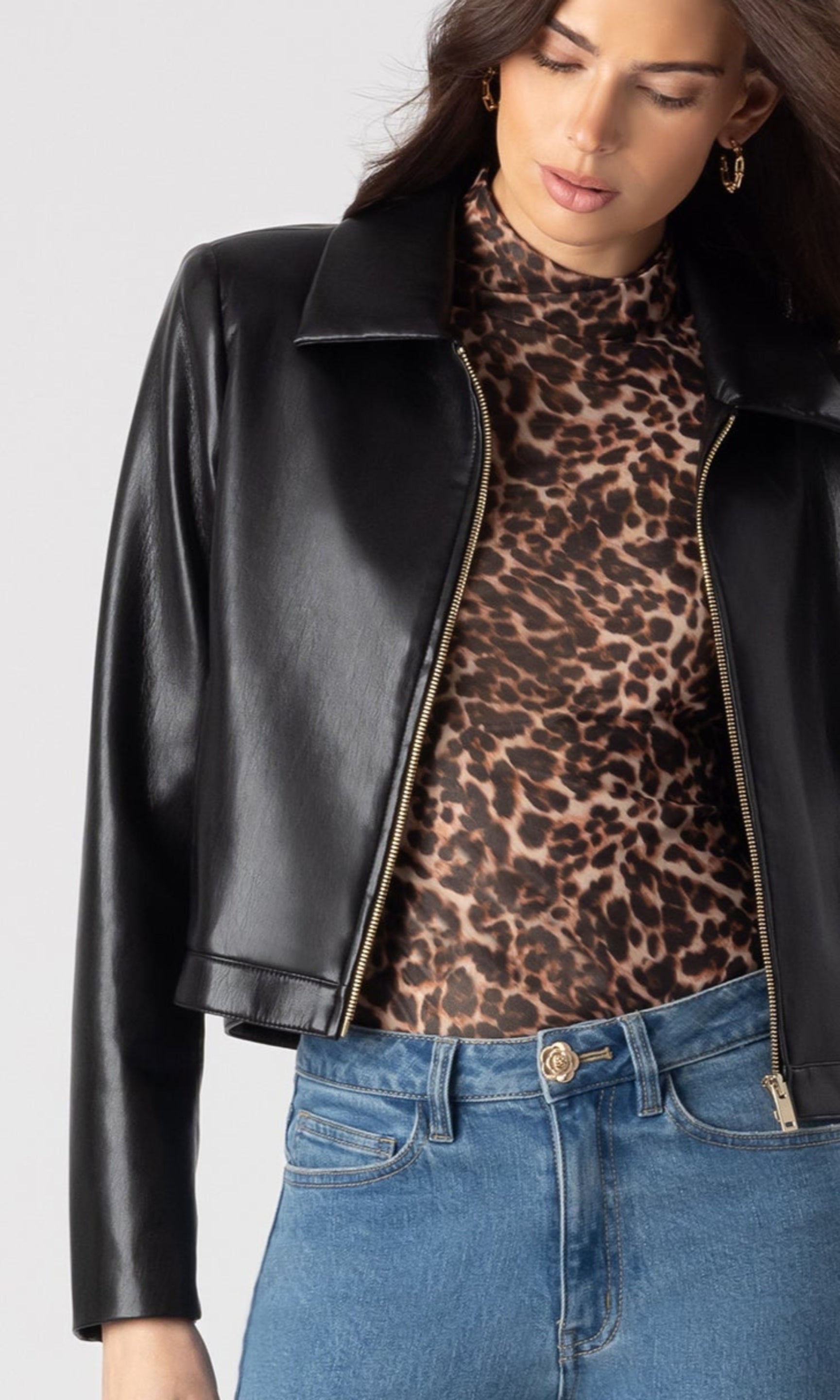 cropped zoomed in image of model wearing the Lola vegan leather jacket in black over a leopard print blouse and paired with blue denim jeans