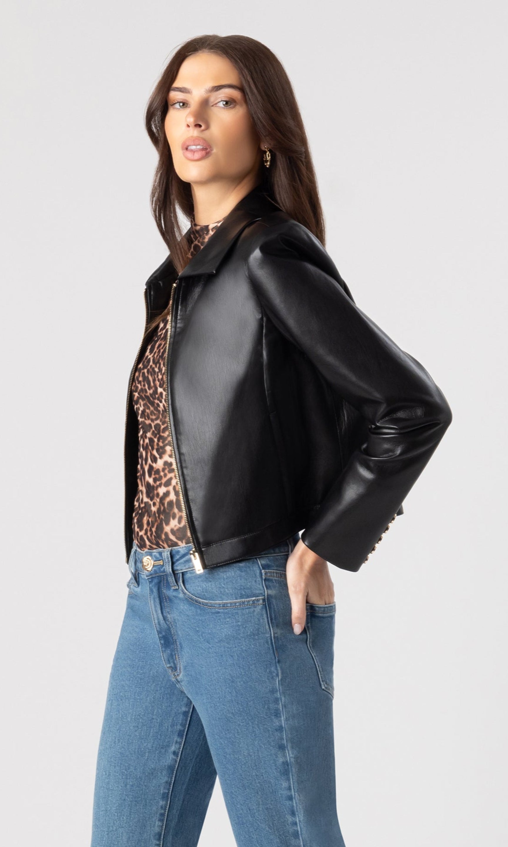 side view image of model wearing the Lola vegan leather jacket in black over a leopard print blouse and paired with blue denim jeans
