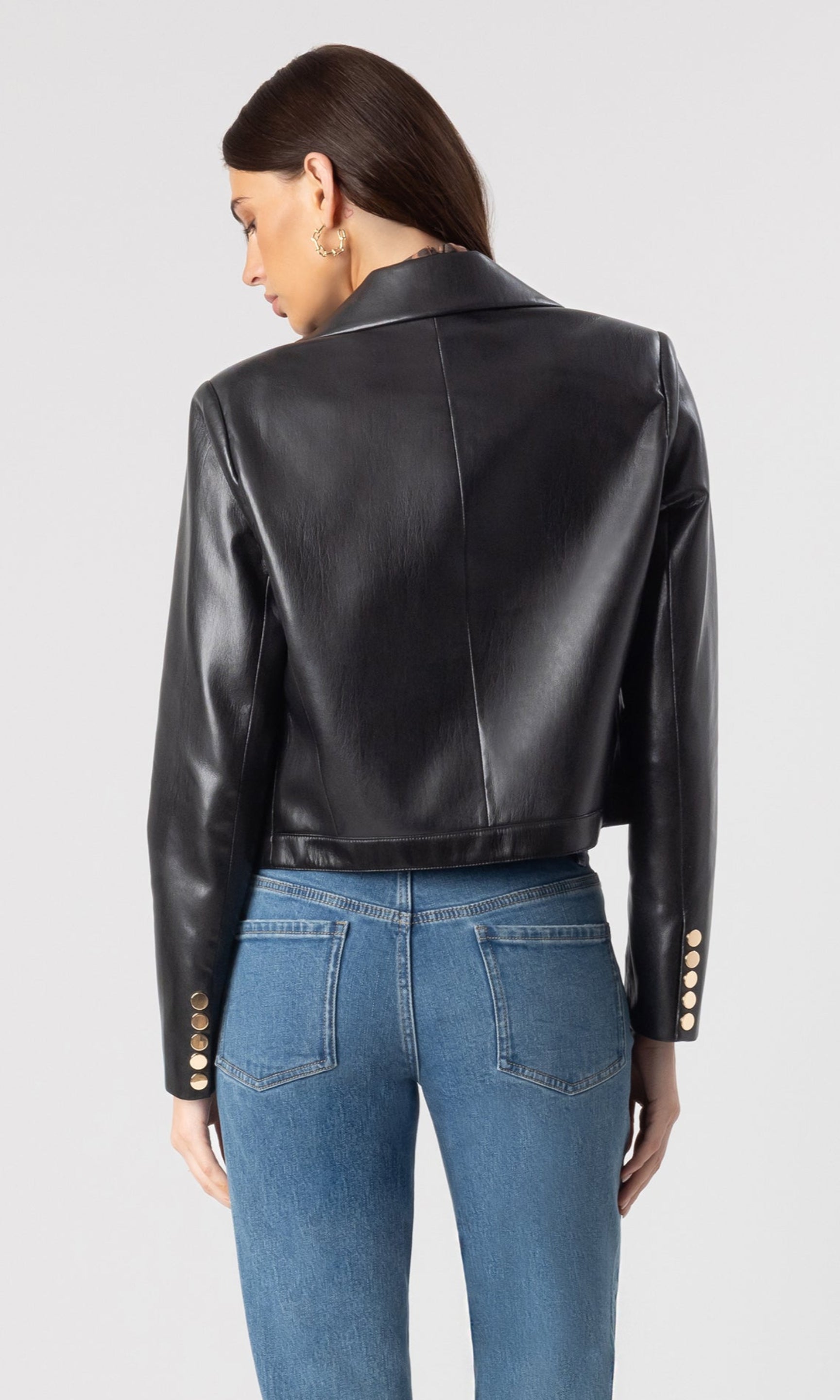 back view image of model wearing the Lola vegan leather jacket in black over a leopard print blouse and paired with blue denim jeans