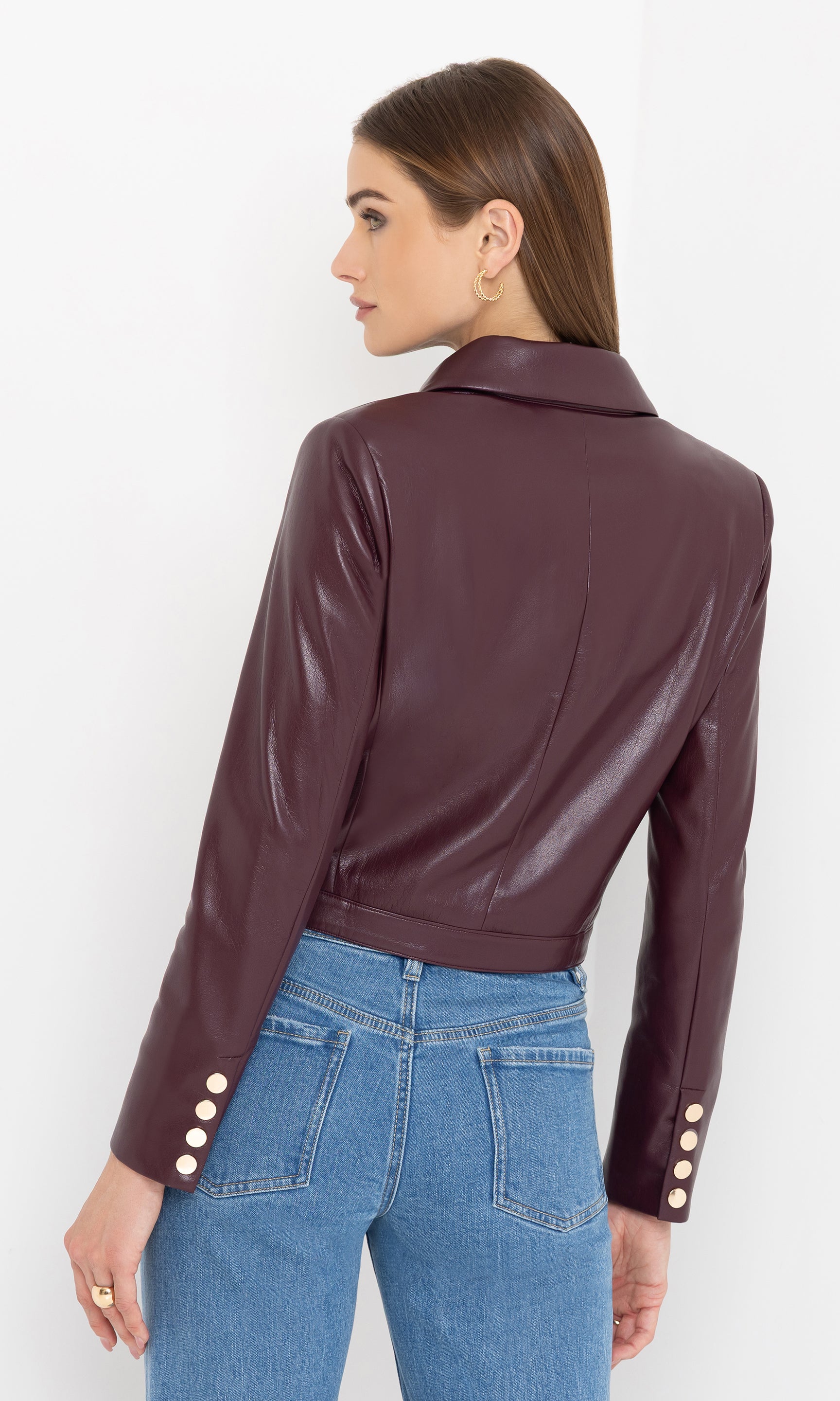 Woman wearing a cabernet vegan leather jacket with gold buttons on a white background