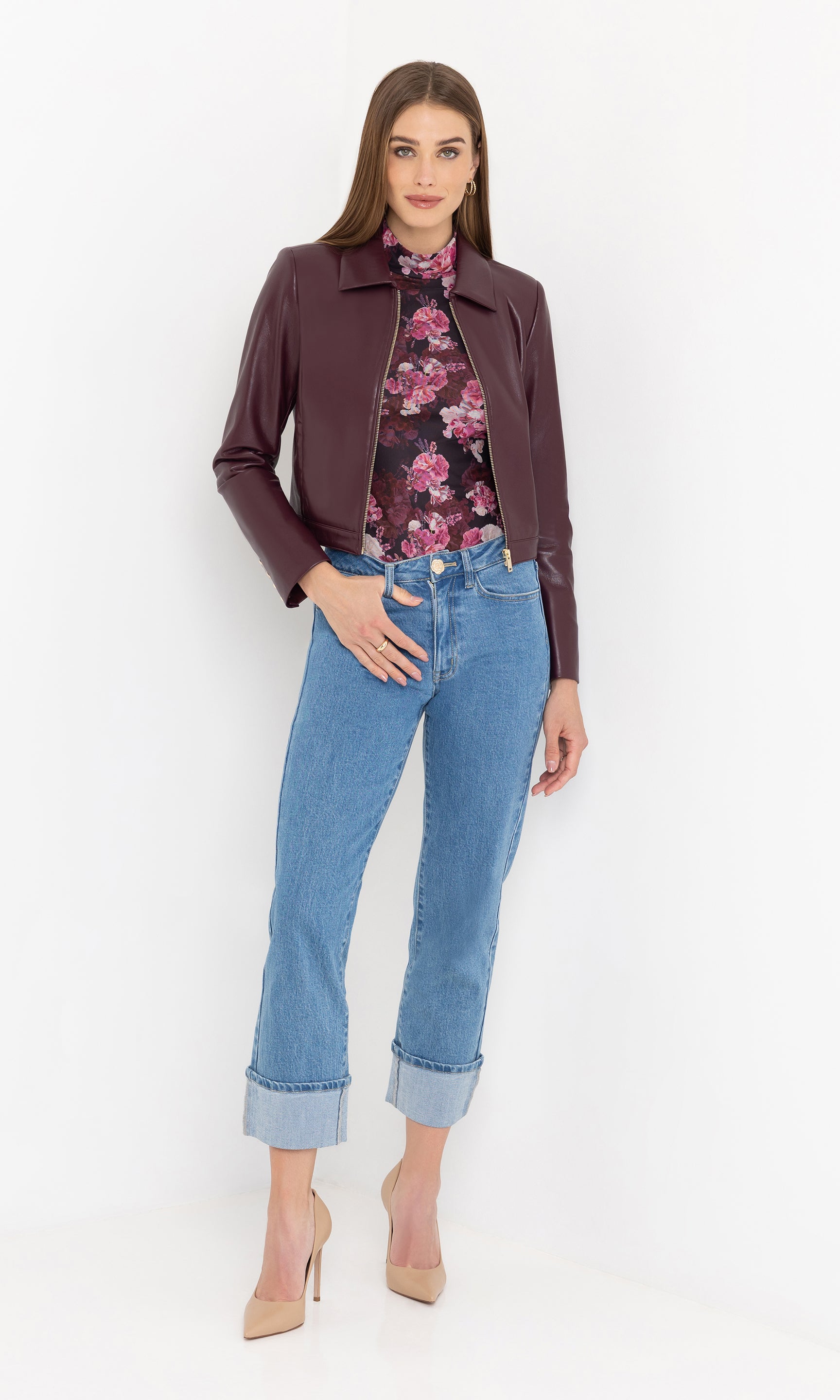 Woman wearing a cabernet vegan leather jacket, floral top, and blue jeans on a white background