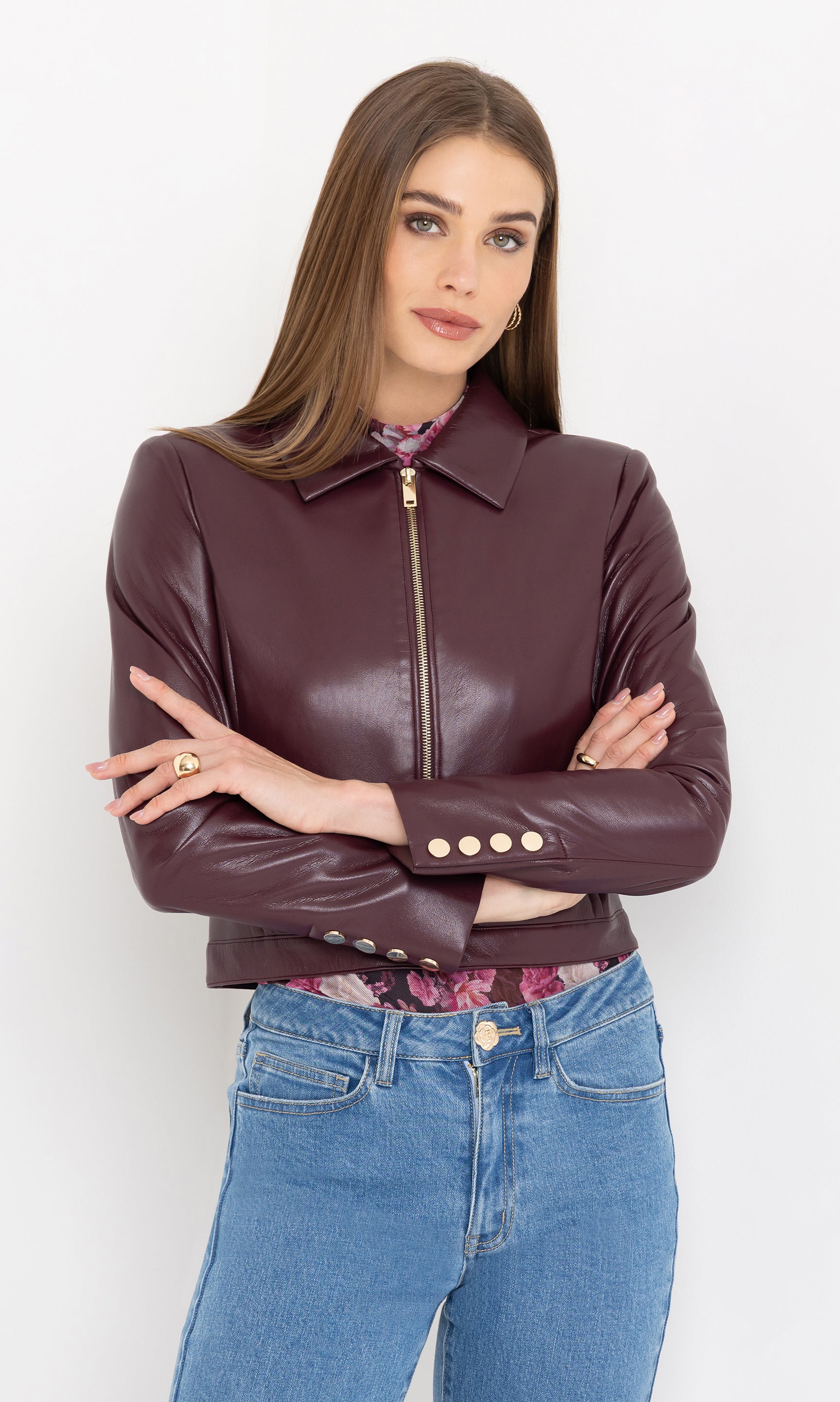 Woman wearing a cabernet vegan leather jacket and blue jeans against a white background