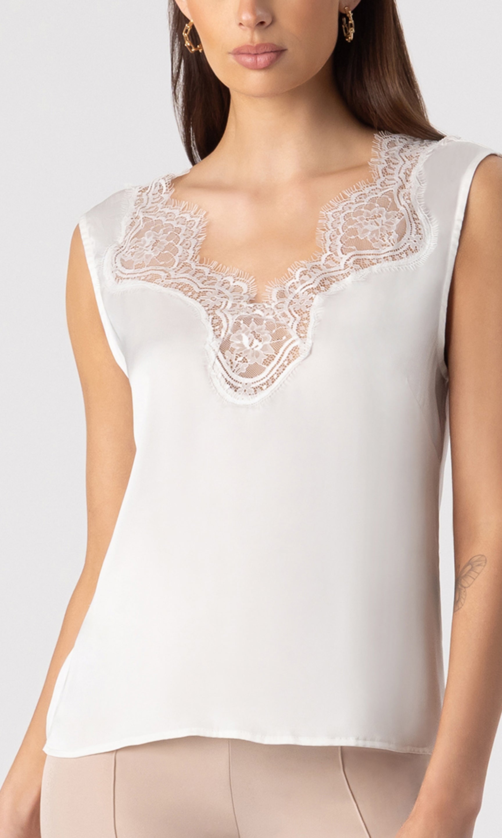 zoomed in image of model wearing the Gladis tank in white showcasing the lace neckline pattern, paired with beige trousers