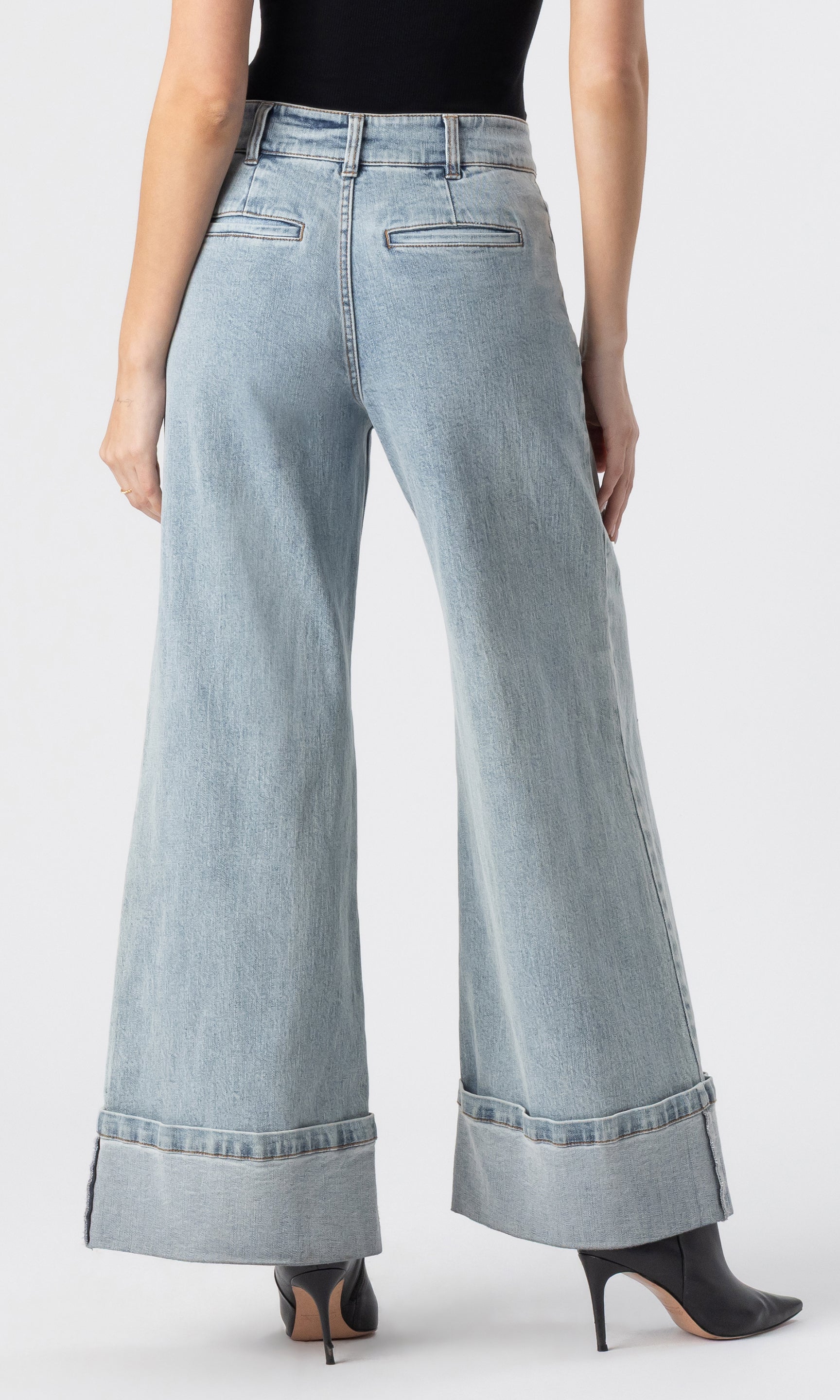cropped back view image of model wearing the Raquel denim jeans in light blue, paired with a black tank and black heeled booties