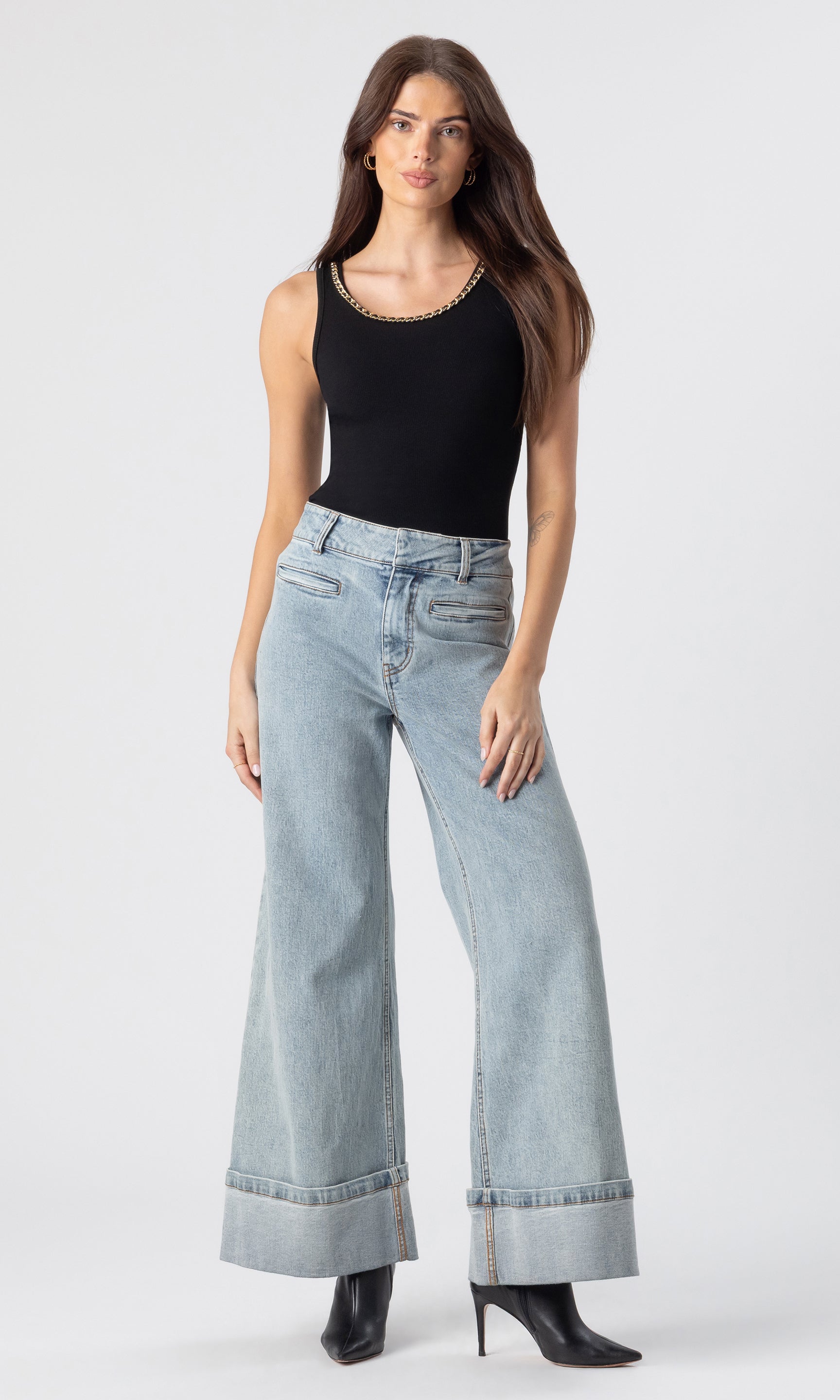 full body image of model wearing the Mabel tank in black with a chain embellished neckline paired with light blue jeans and black heeled booties