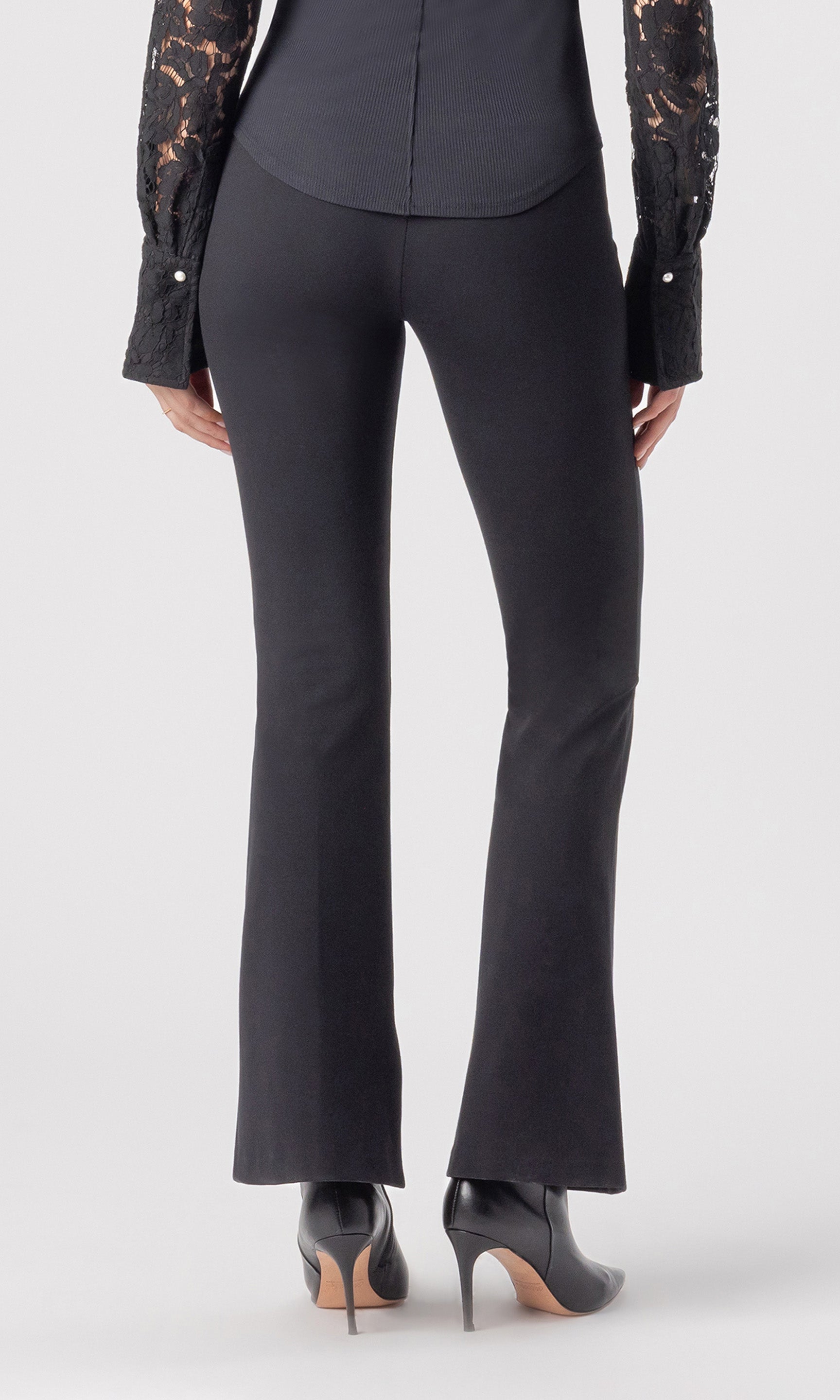 cropped back view image of model wearing the Murray Ponte Leggings in black, paired with a black blouse and black heeled booties