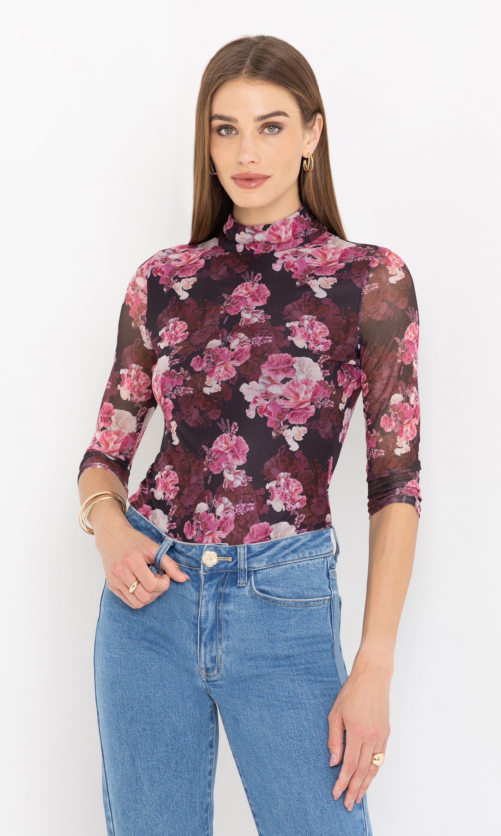 Woman wearing a floral mesh top and blue jeans against a white background