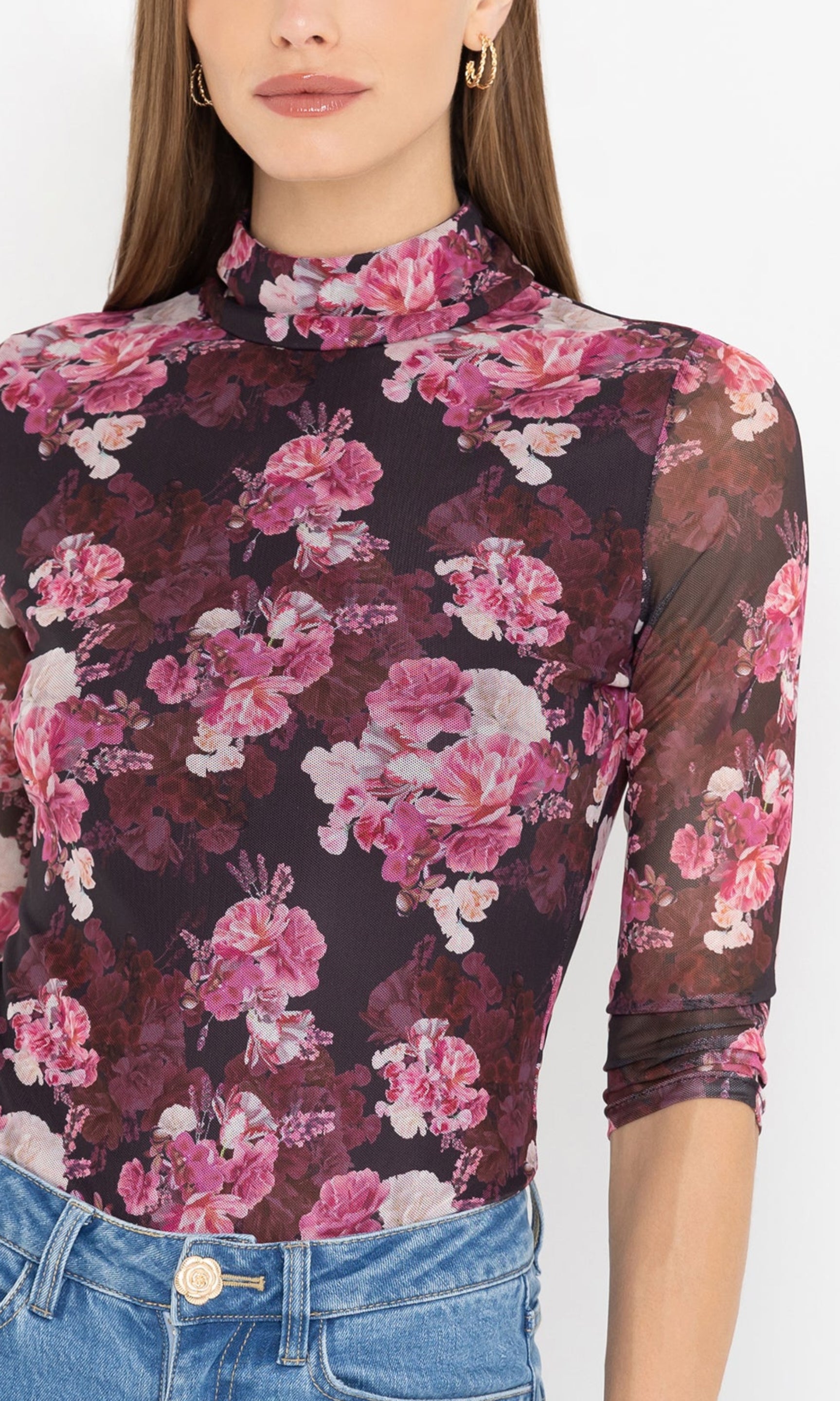 Detailed image of woman wearing a floral long-sleeve top and blue jeans on a white background, showcasing the beautiful burgundy floral print