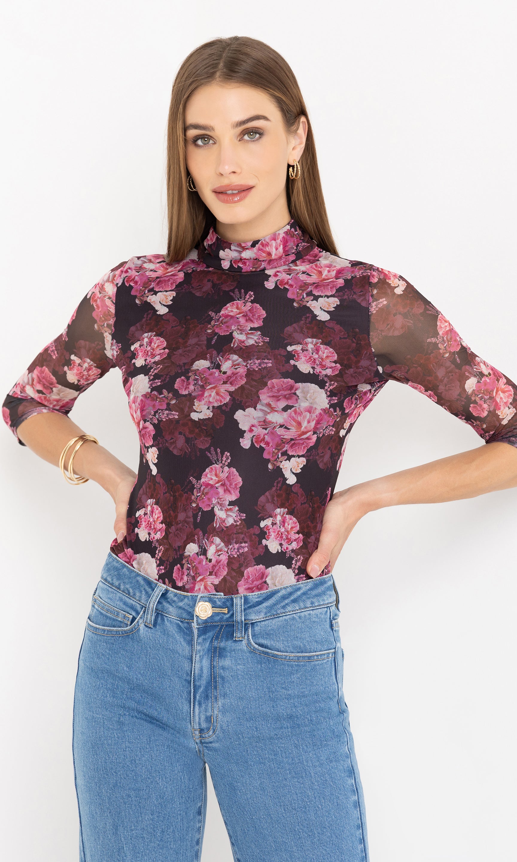 Woman wearing a floral blouse with a white background with her hands on her hips, paired with blue jeans