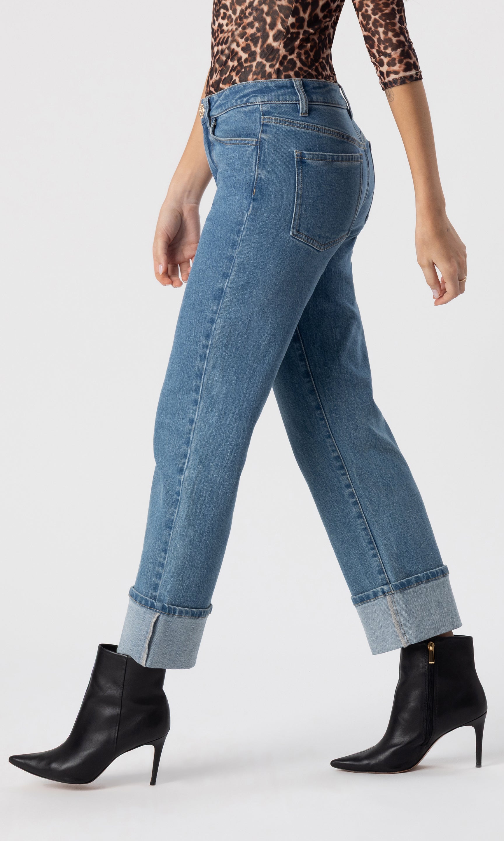 cropped side view image of model wearing the Rylan Denim Jeans with folded cuffed legs, paired with a leopard print top and black heeled booties