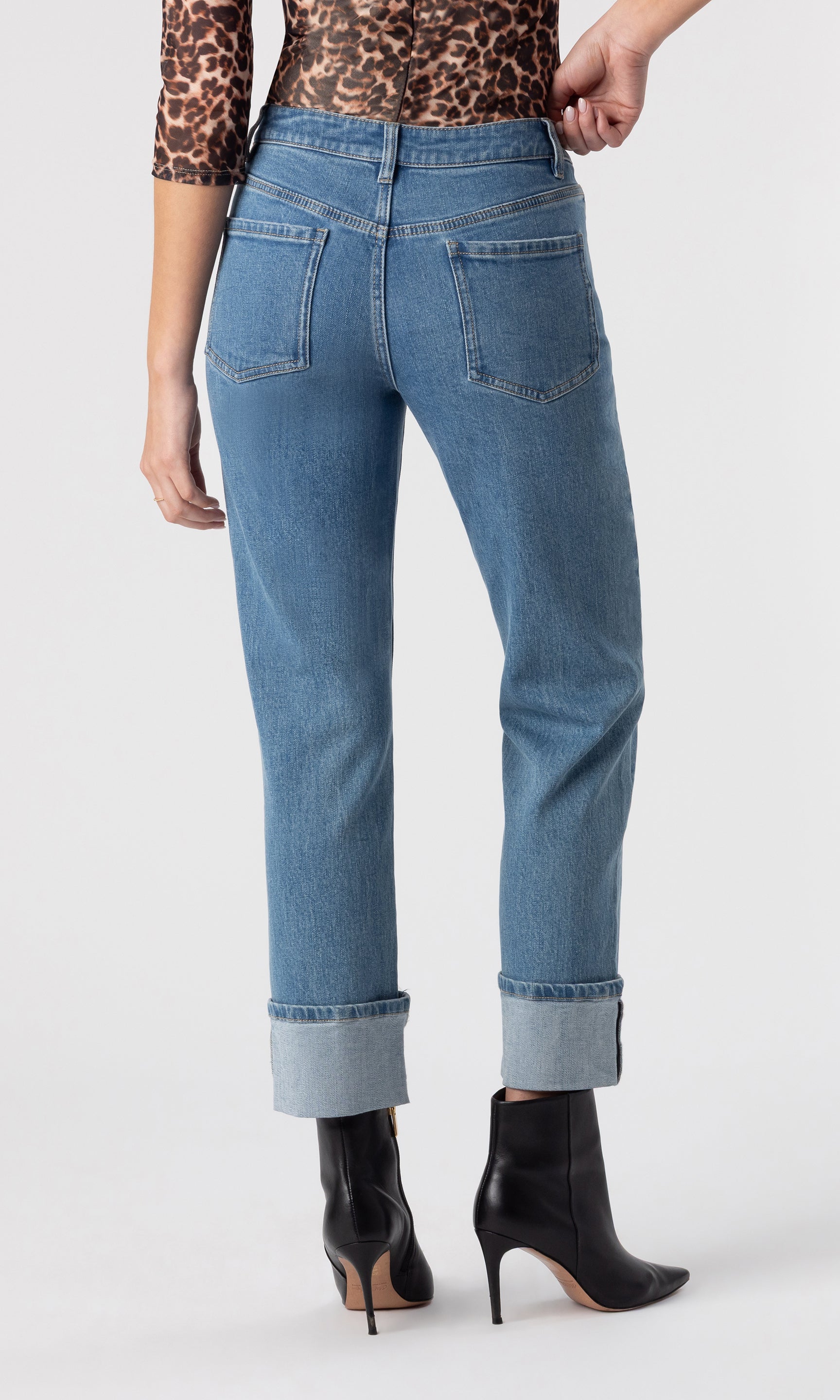 cropped back view image of model wearing the Rylan Denim Jeans with folded cuffed legs, paired with a leopard print top and black heeled booties