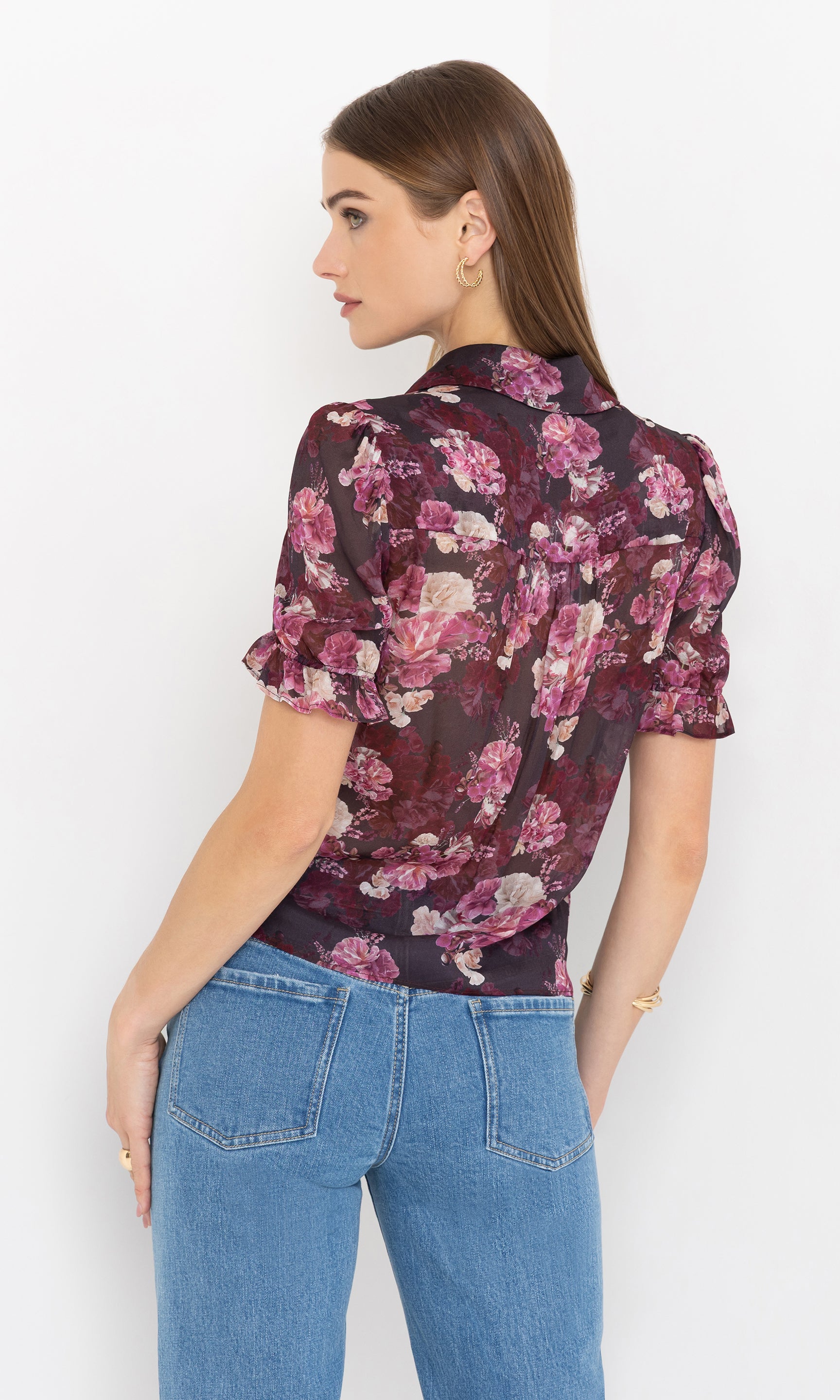 Back view image of model wearing a floral blouse and blue jeans on a white background