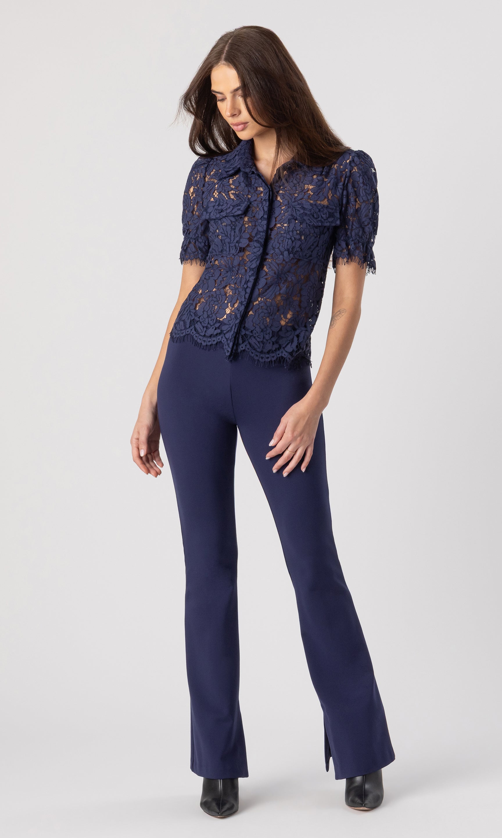 full body image of model posed looking down wearing the Mina lace shirt in navy paired with matching navy leggings and black heels