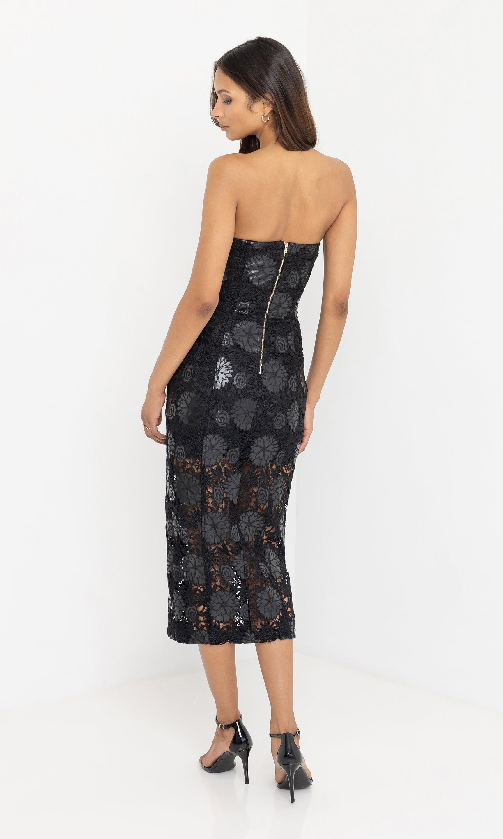 Back view of woman wearing a black floral vegan leather strapless dress on a white background