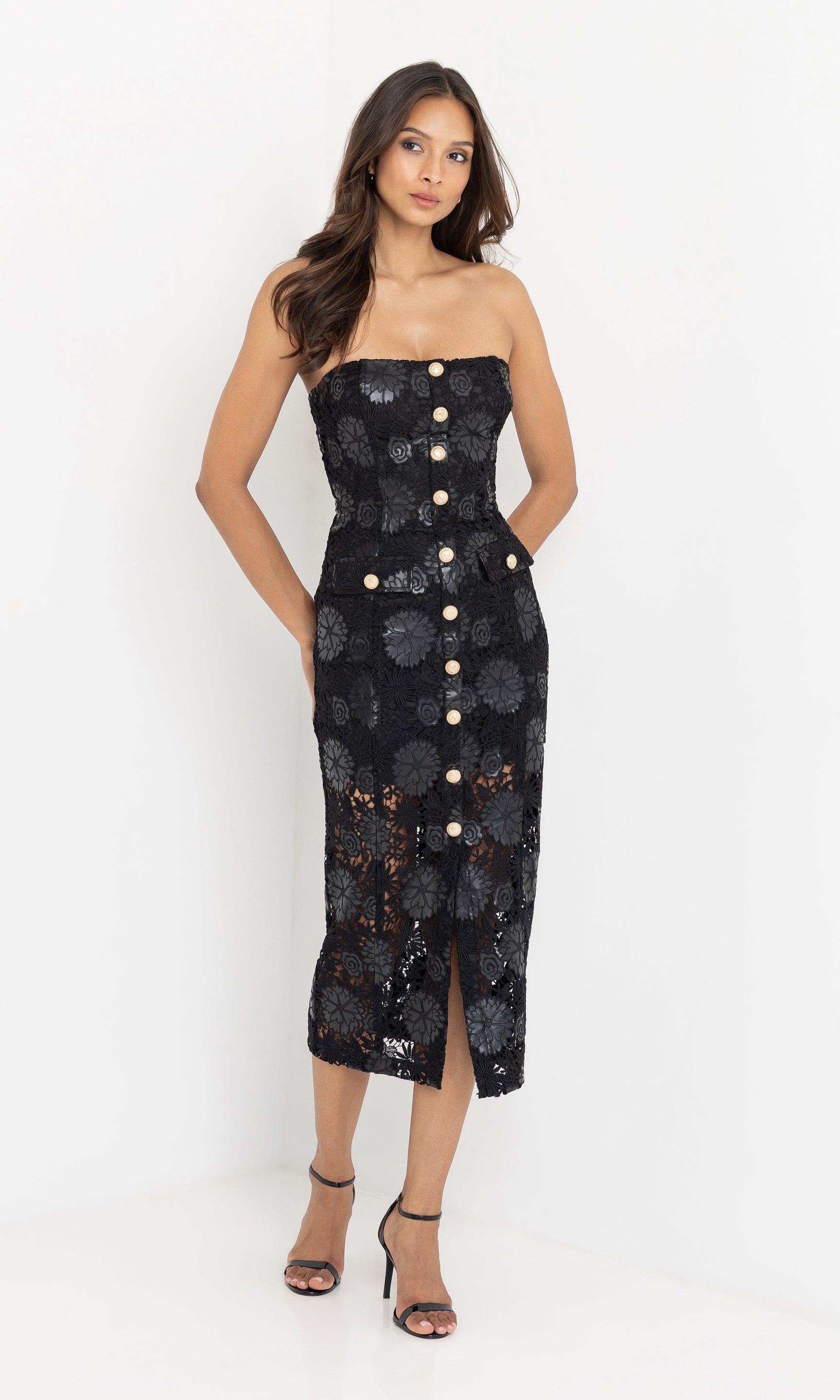 Woman wearing a black vegan leather strapless dress with floral patterns and gold buttons on a white background