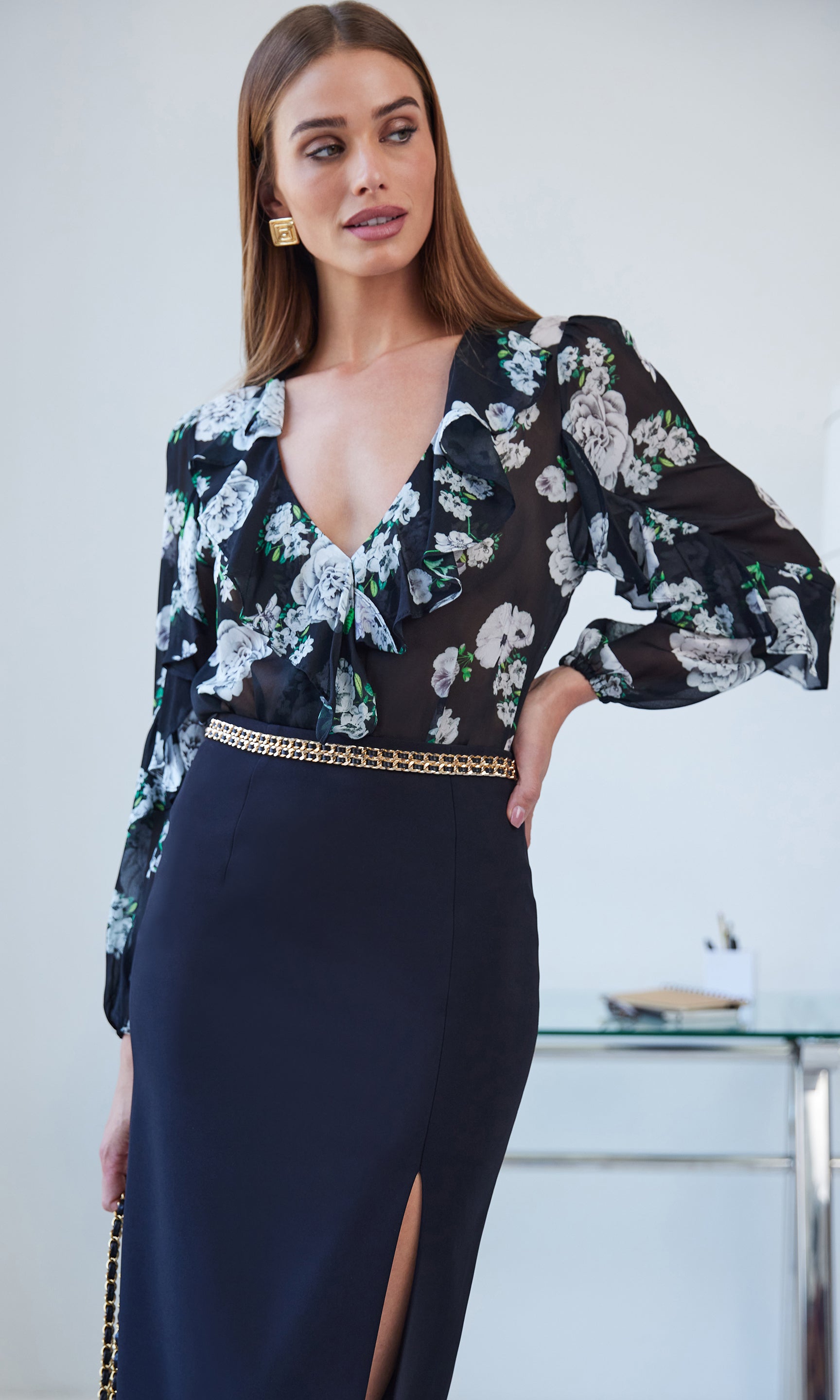 Woman wearing a floral blouse over a black pencil skirt with a slit, standing indoors.