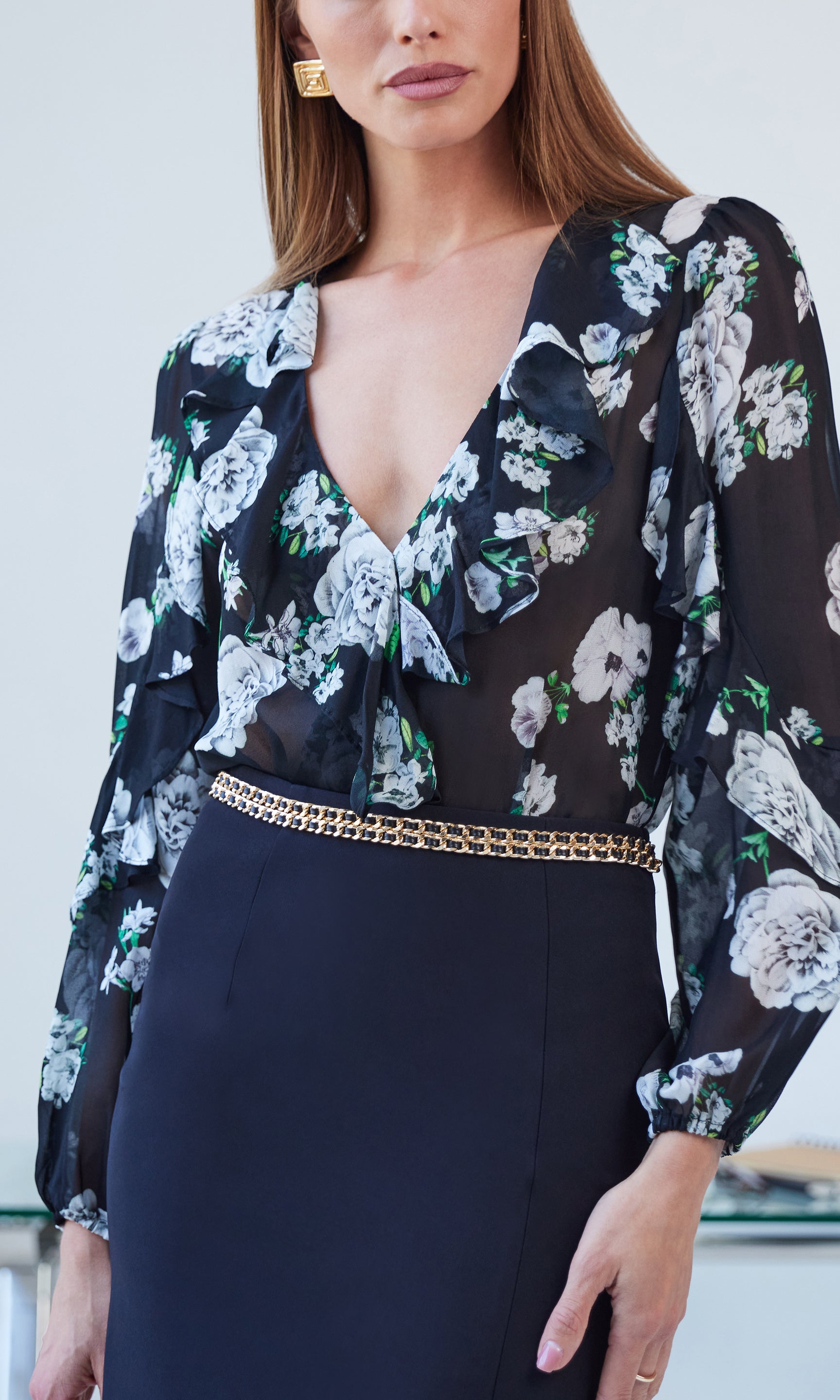 Woman wearing a floral blouse with a deep neckline and a gold belt.