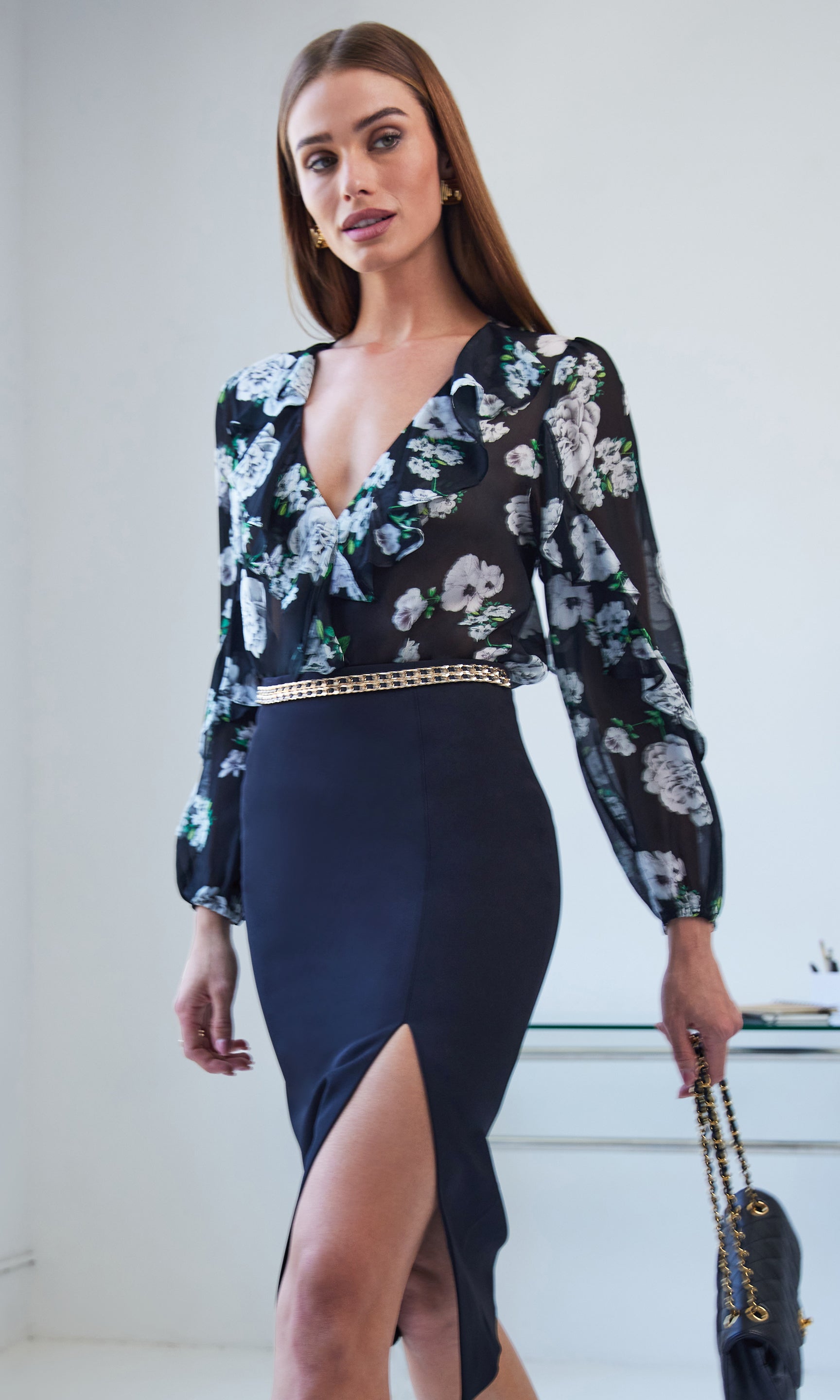 Woman wearing a floral blouse and black pencil skirt with a white background