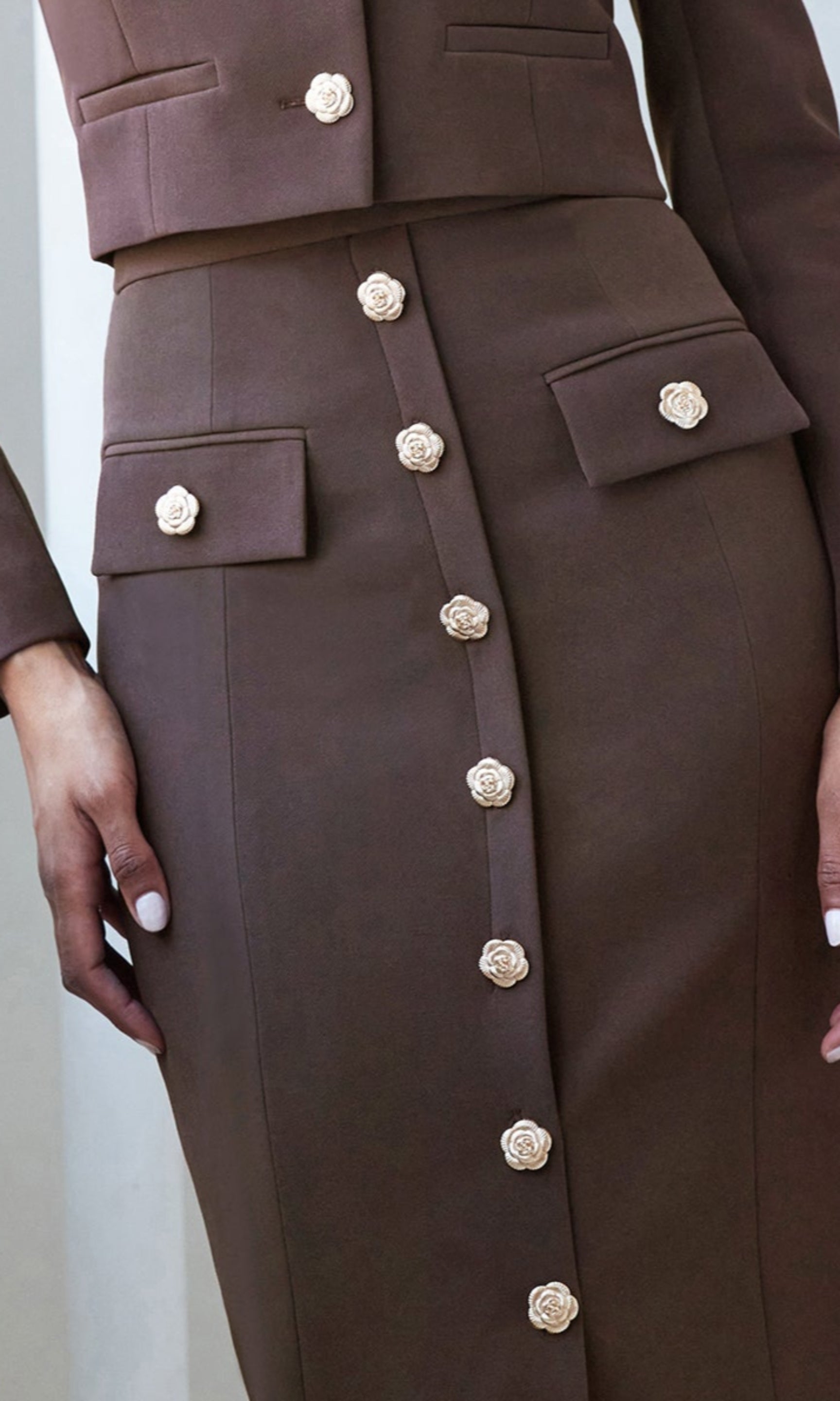 Zoomed in image of model wearing a brown crepe set with closed in details on the skirt gold floral buttons