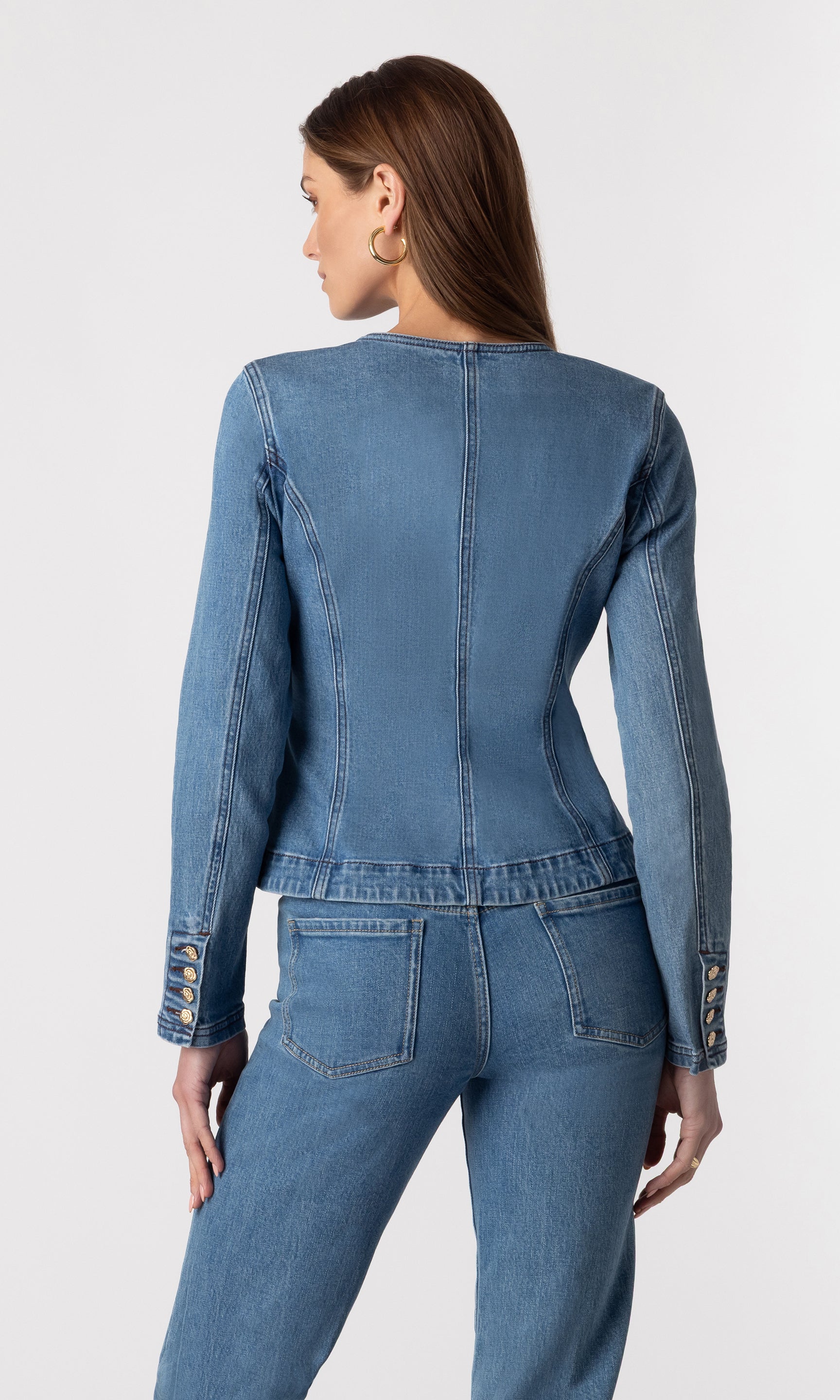 back view of model wearing the Ophelia blue denim jacket showing the buttons on the cuff of the jacket's sleeves, paired with matching blue denim jeans