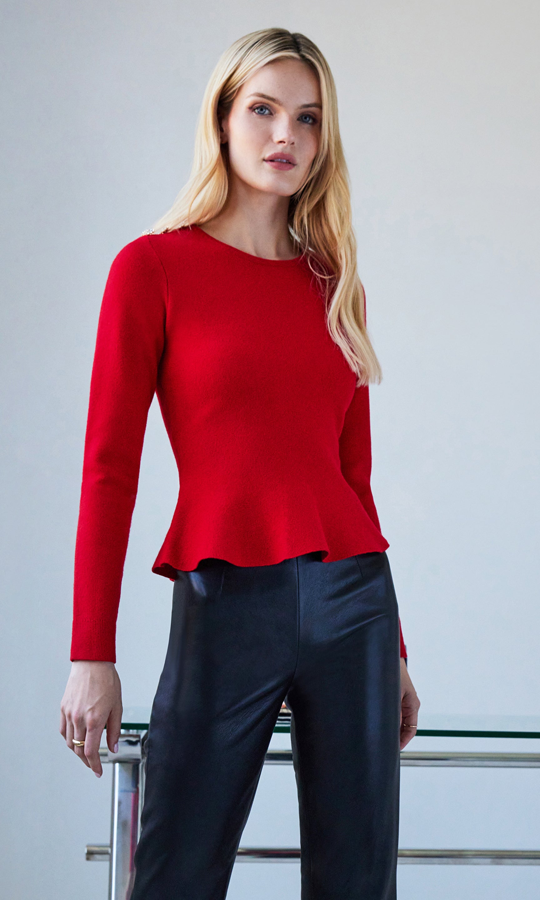 Woman wearing a red peplum top and black pants against a gray background
