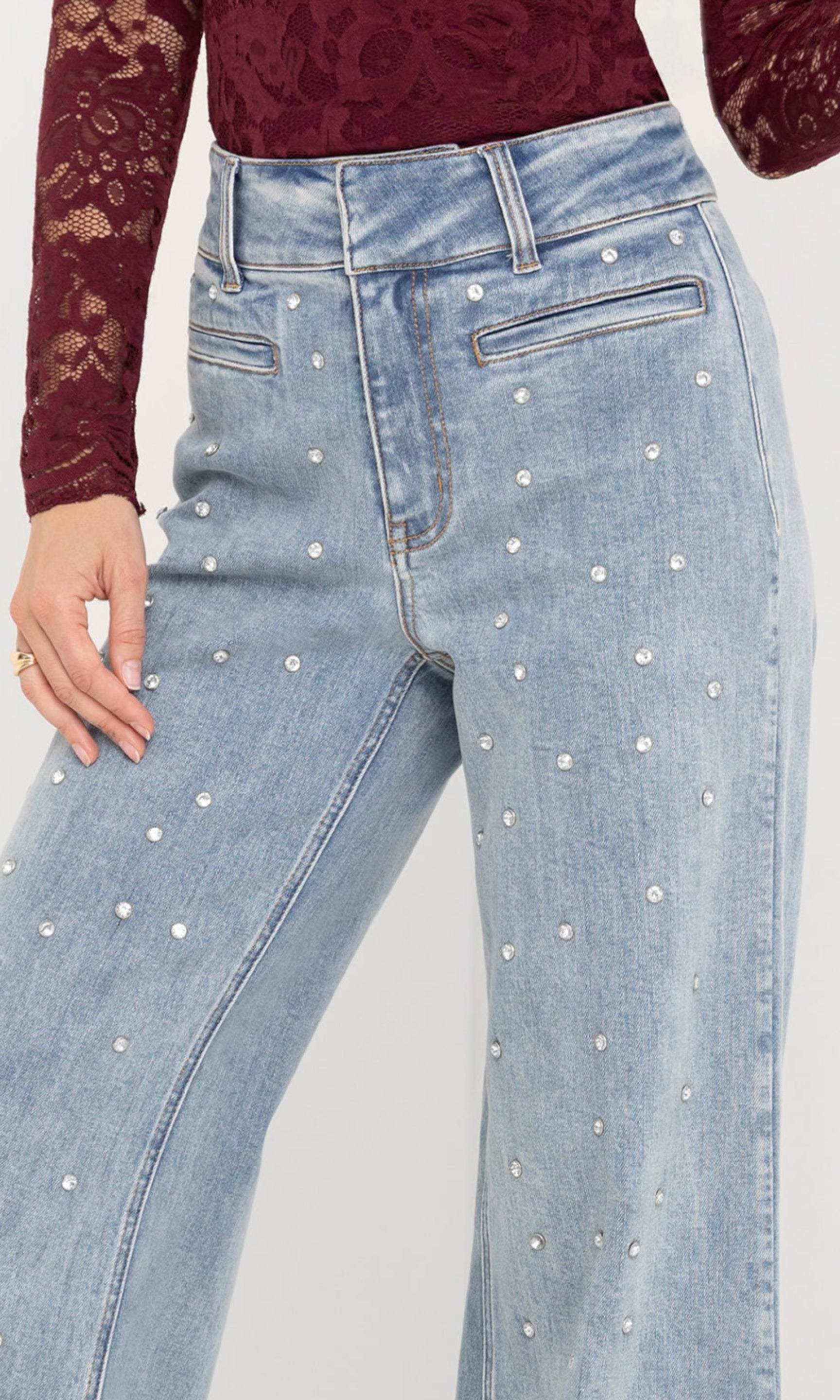 Light blue jeans with crystal embellished details worn by a person on a white background