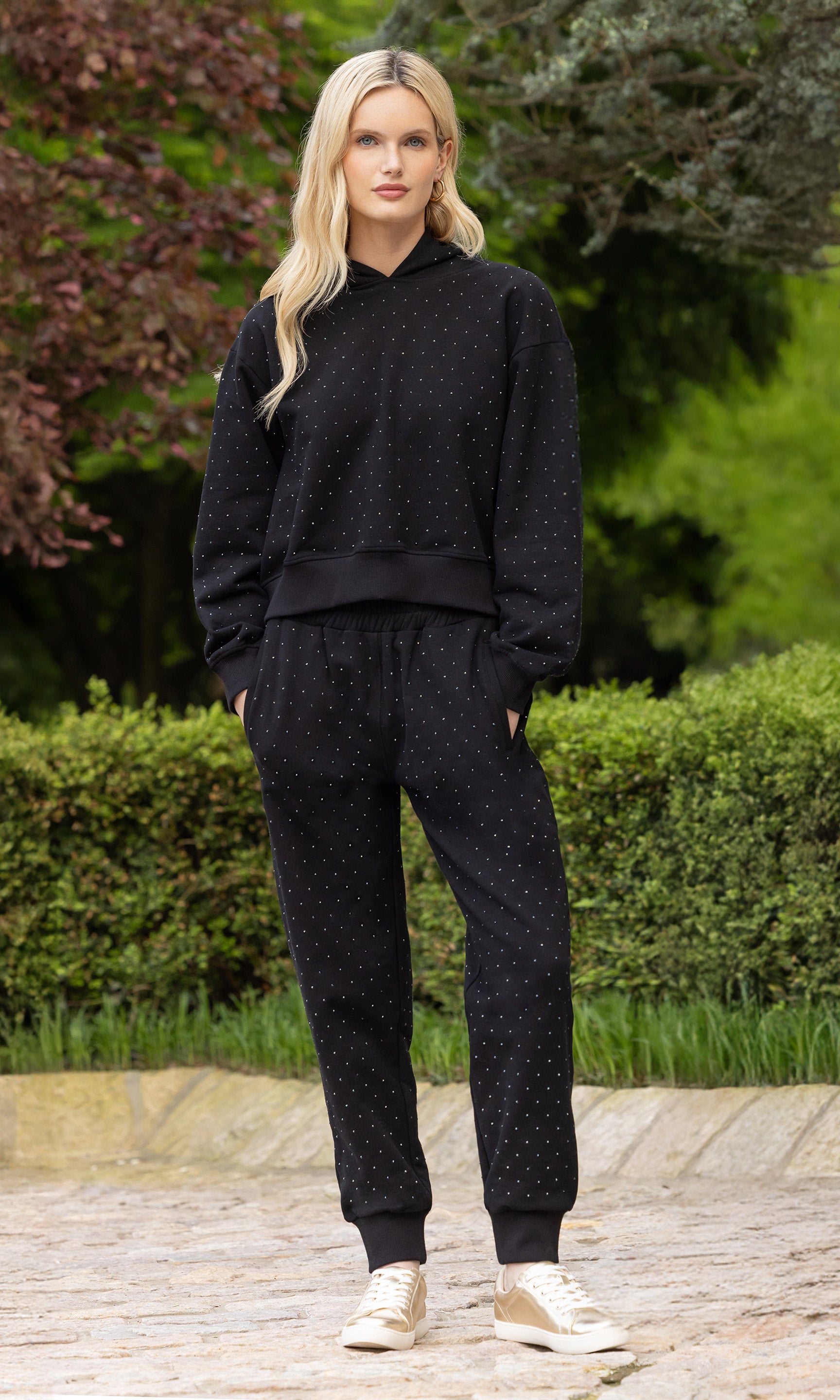 image of model posing in an outdoor patio wearing a black sweatsuit embellished in crystals all over, paired with sneakers