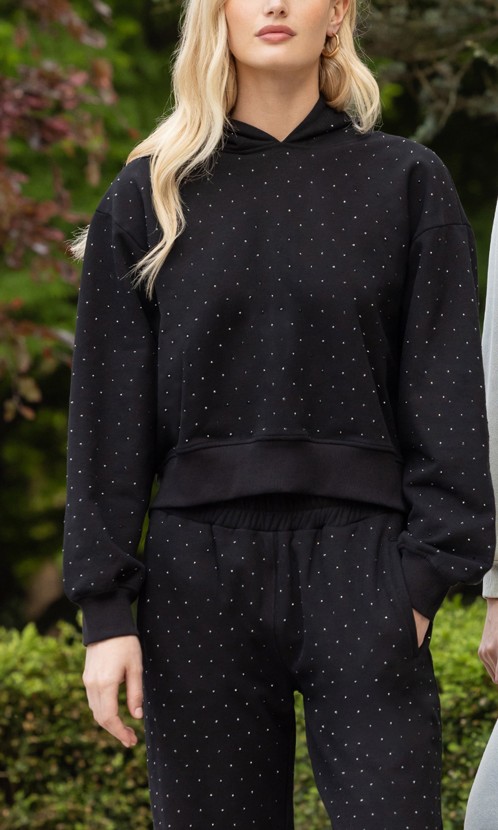 cropped in image of model posing in an outdoor patio wearing a black sweatsuit showcasing the embellished in crystals all over
