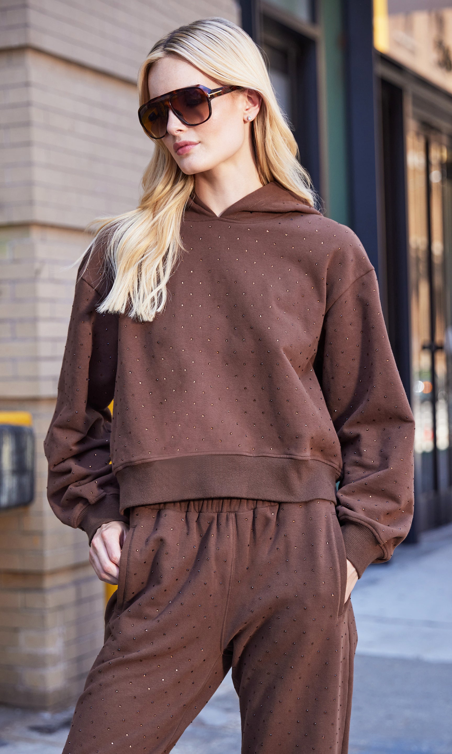 Woman wearing a brown sweatsuit and sunglasses on a city street.