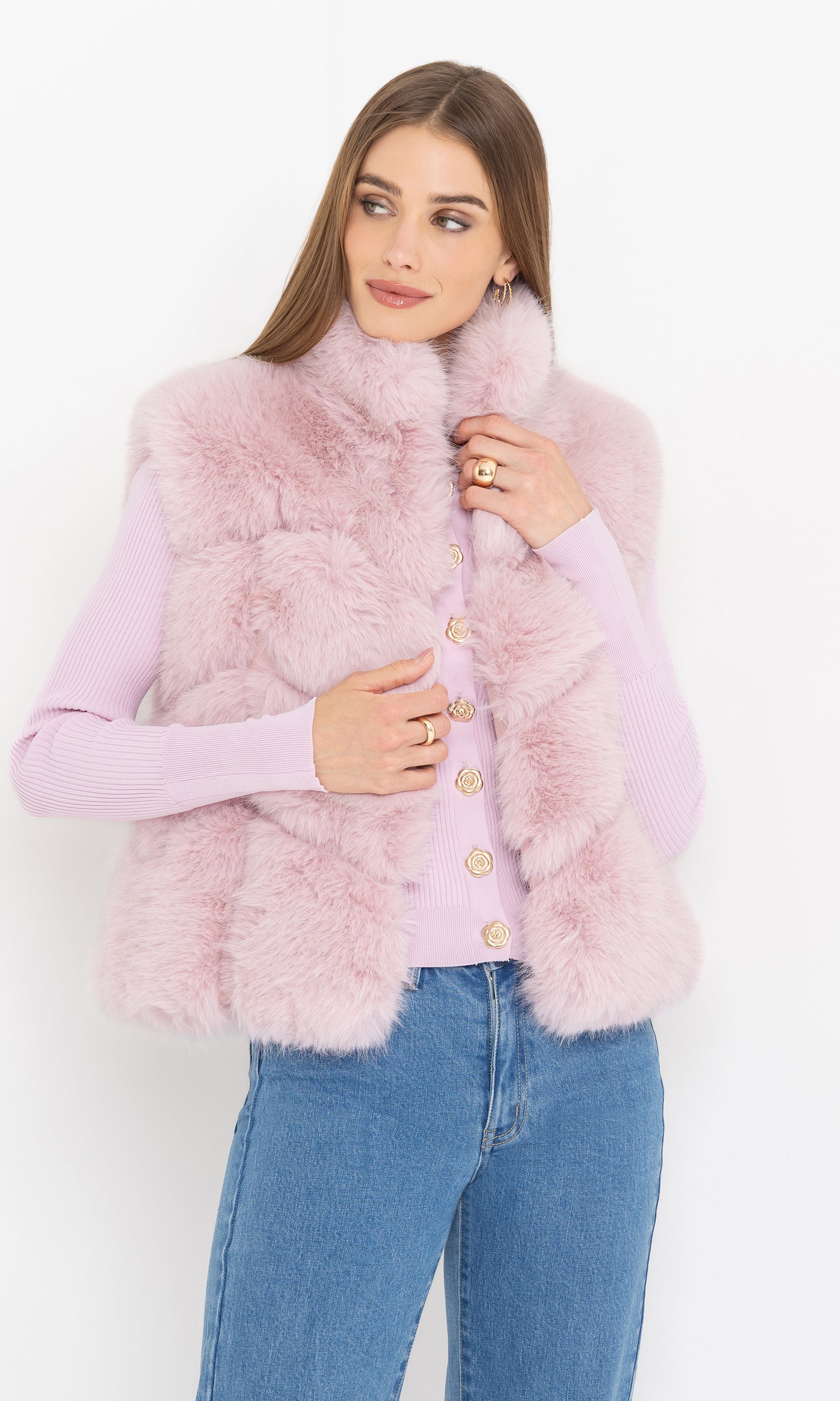 Woman wearing a pink fluffy faux fur vest over a light pinksweater with a white background