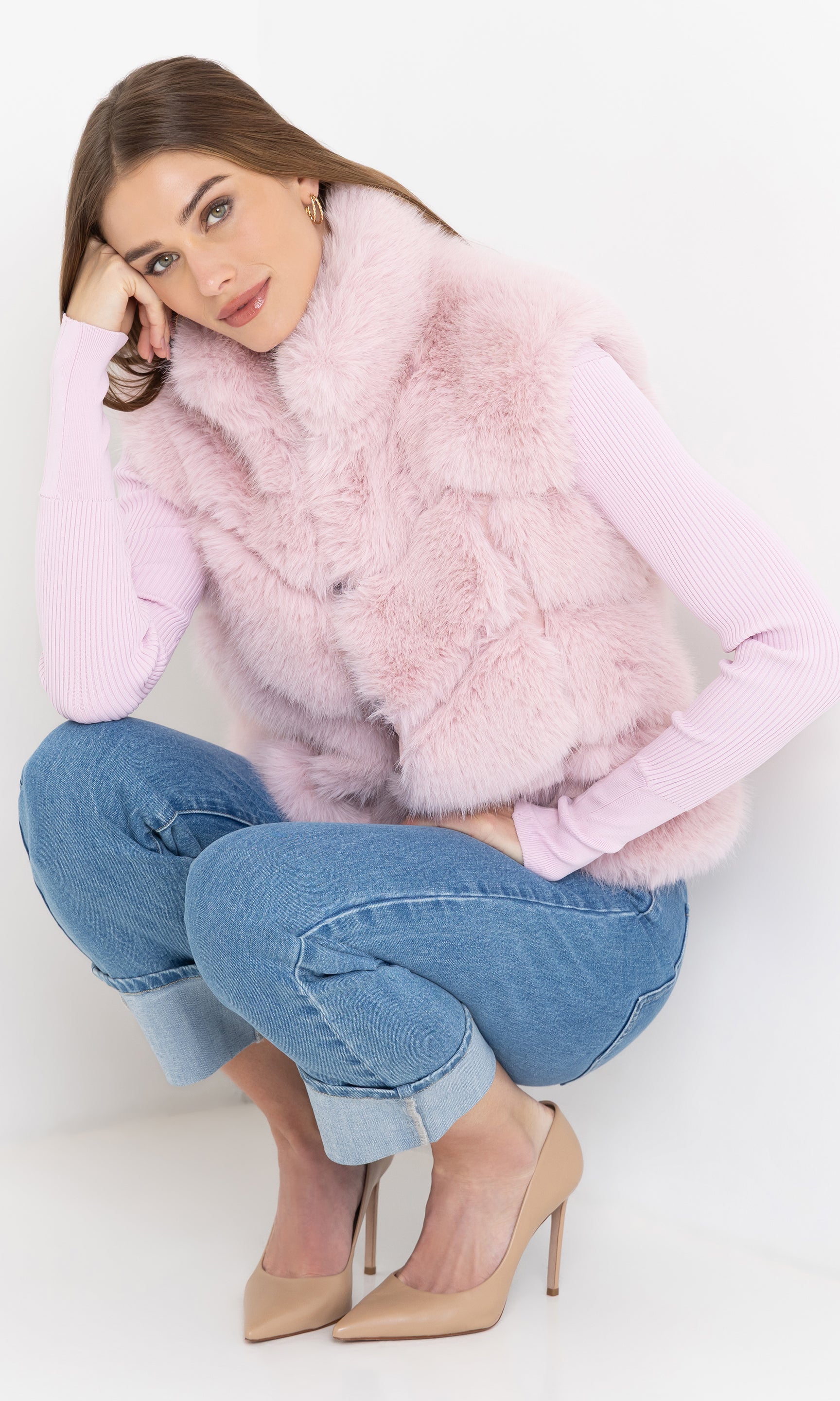 Seated angled view of Rosario Faux Fur Vest in blush pink, paired with casual blue jeans.