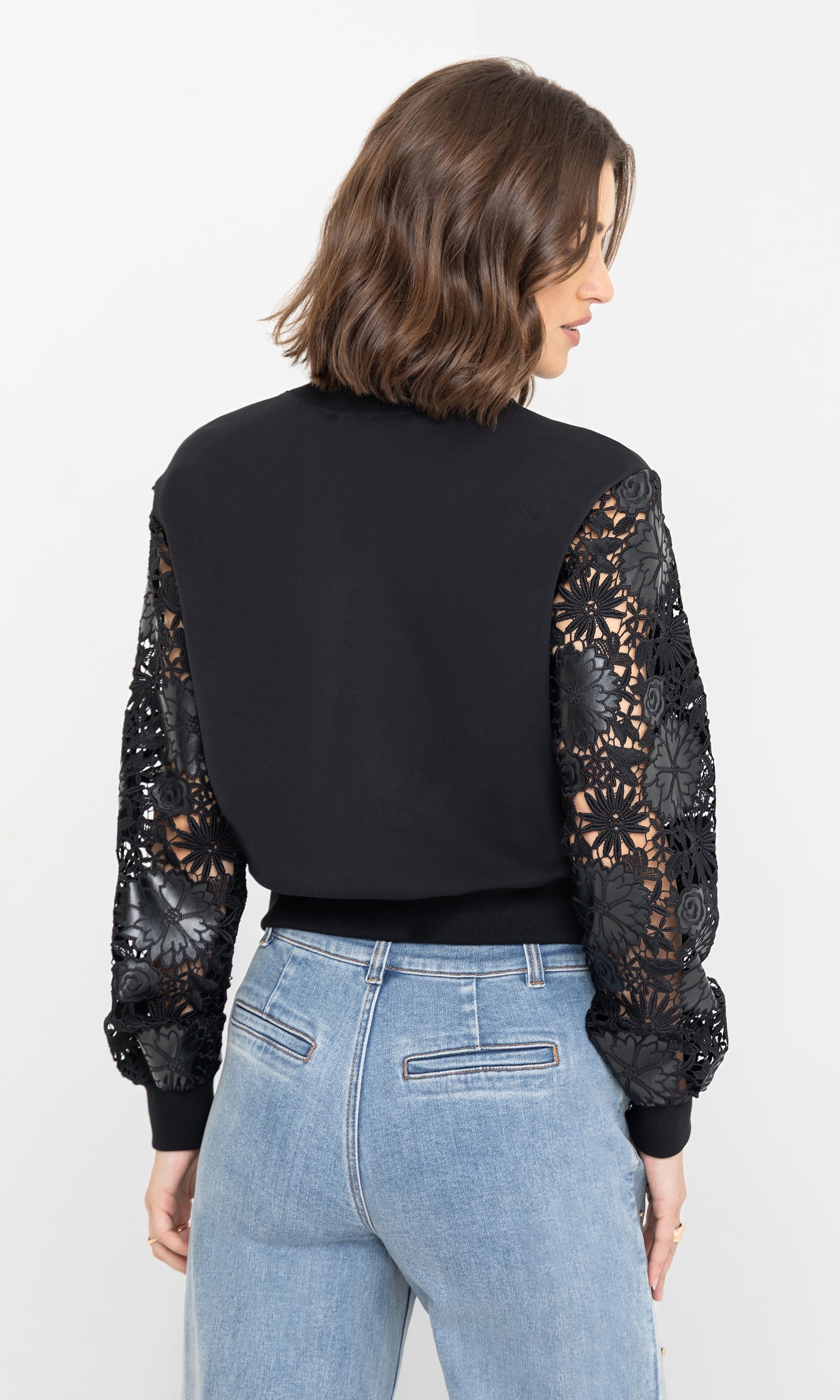 Rear view of the model showing the relaxed fit of the theron guipure combo sleeve sweatshirt with sheer lace sleeves.