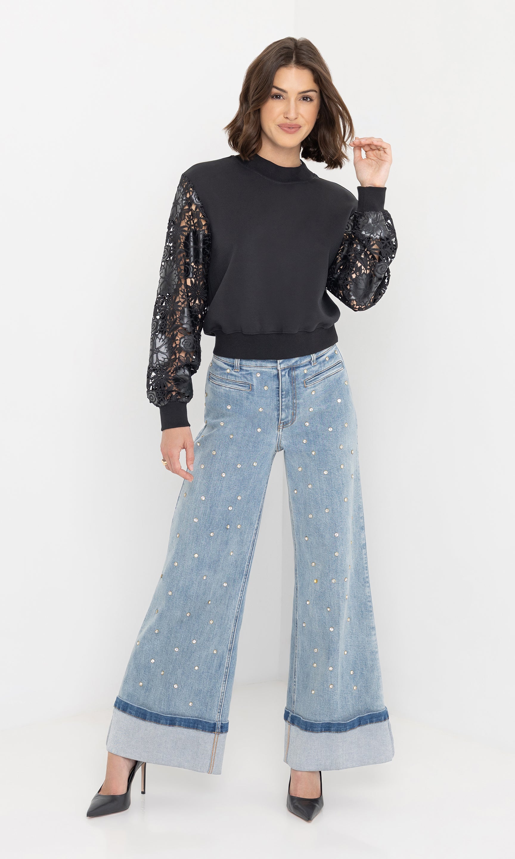 Full body front view of the model wearing the theron guipure combo sleeve sweatshirt in black with crystal-embellished jeans and heels.