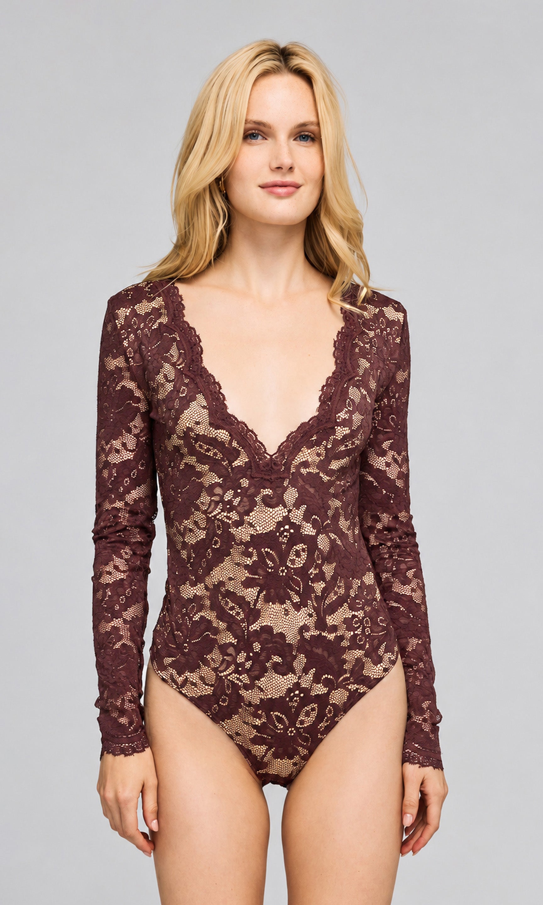 Model wearing a long-sleeve lace bodysuit in a deep burgundy-brown color with a sheer floral lace pattern and a deep V-neckline, on a plain background.