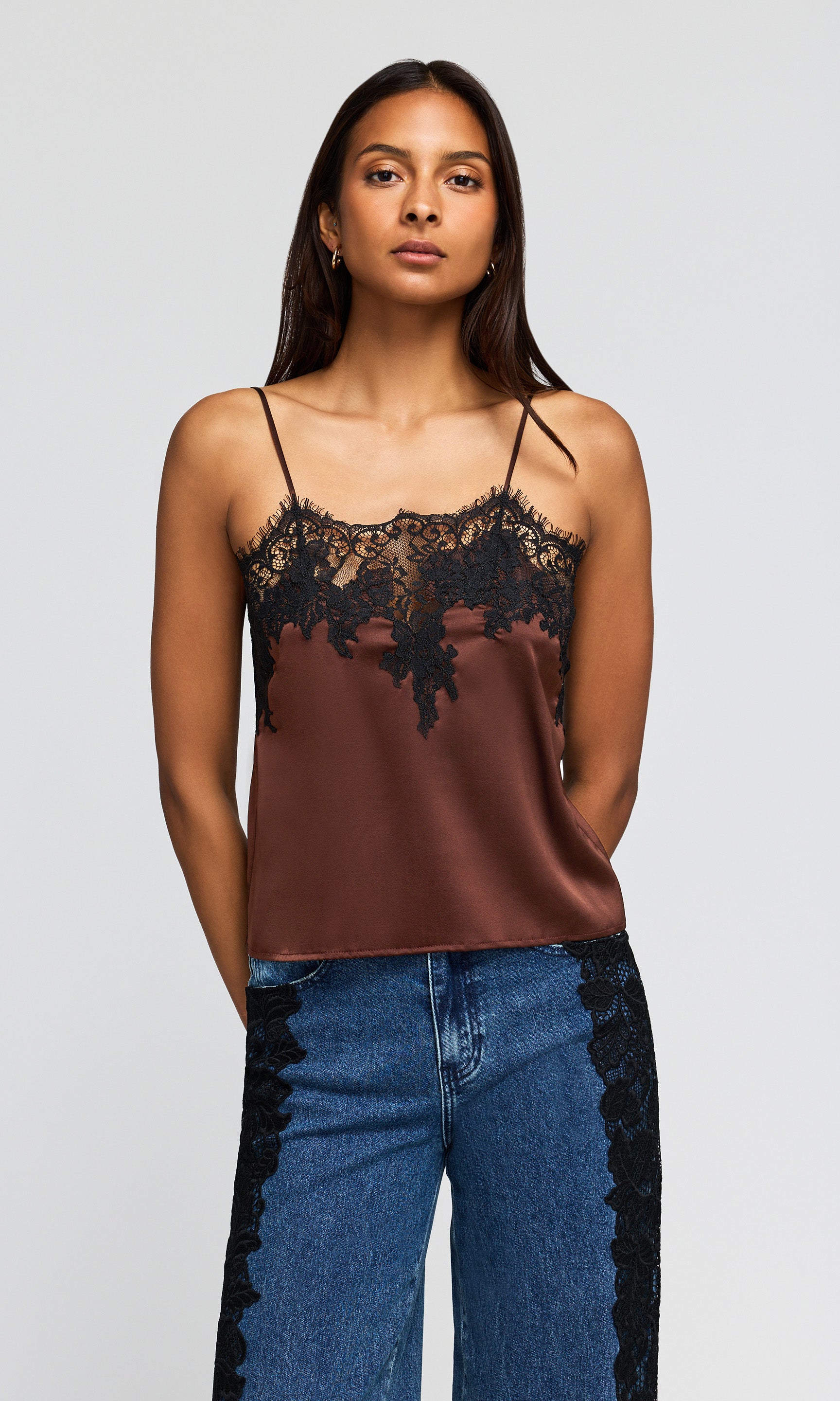 Model wearing a brown satin camisole top with black lace trim along the neckline, paired with blue jeans.