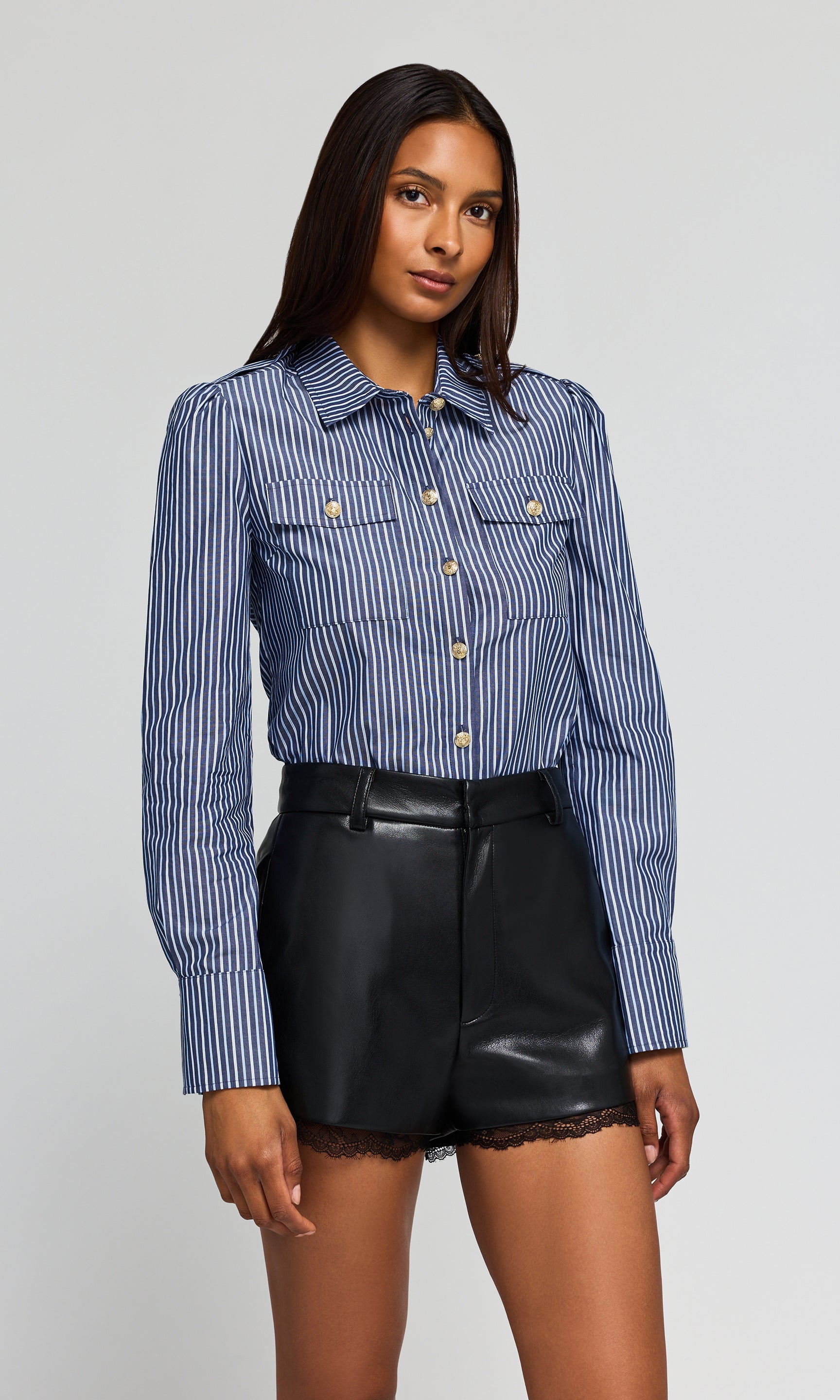 Side view of model wearing a blue and white striped button-up shirt tucked into black shorts, on a plain background.