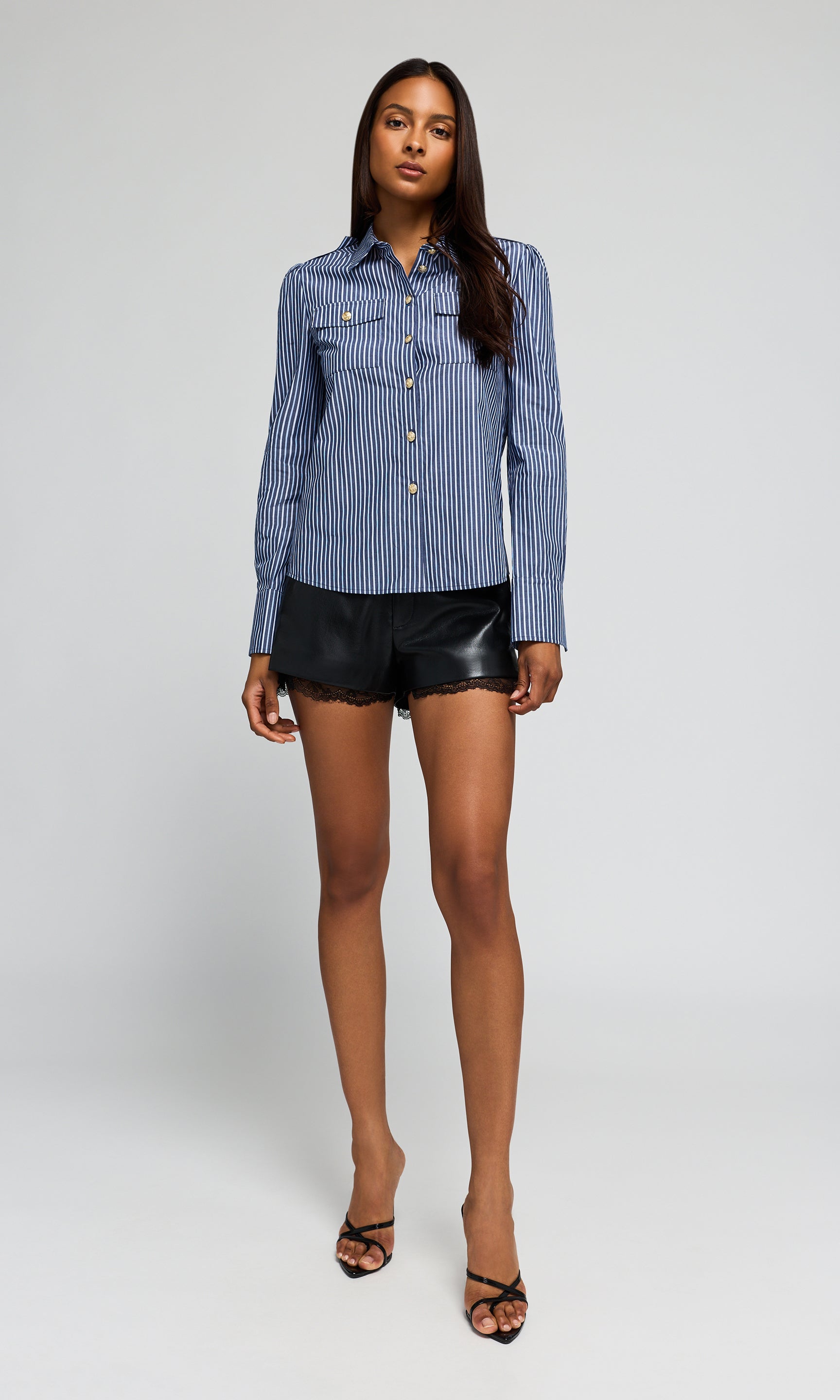 Model wearing a blue and white striped button-up shirt with black leather-look shorts, on a plain background.