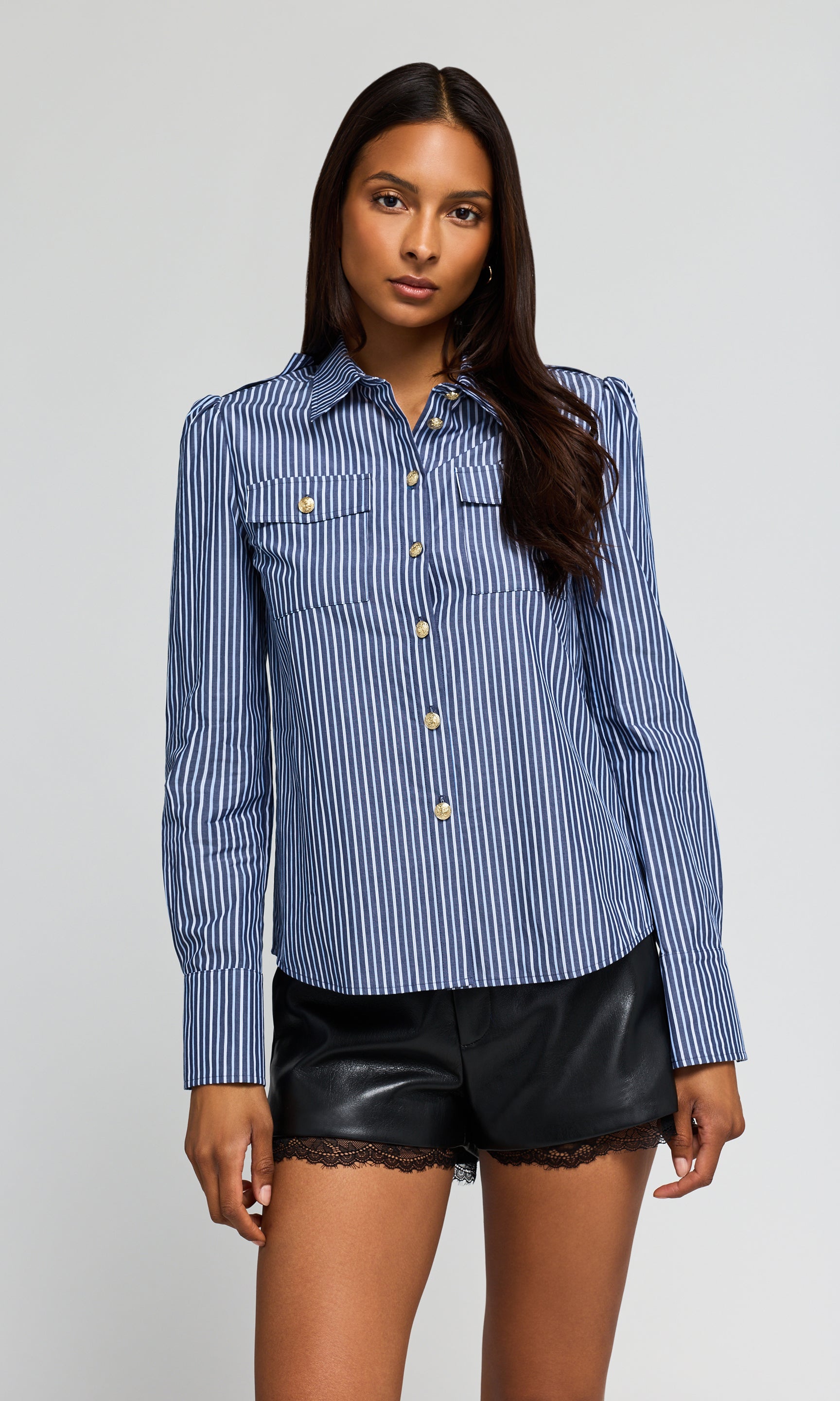 Model wearing a blue and white striped button-up shirt with chest pockets, paired with black shorts.