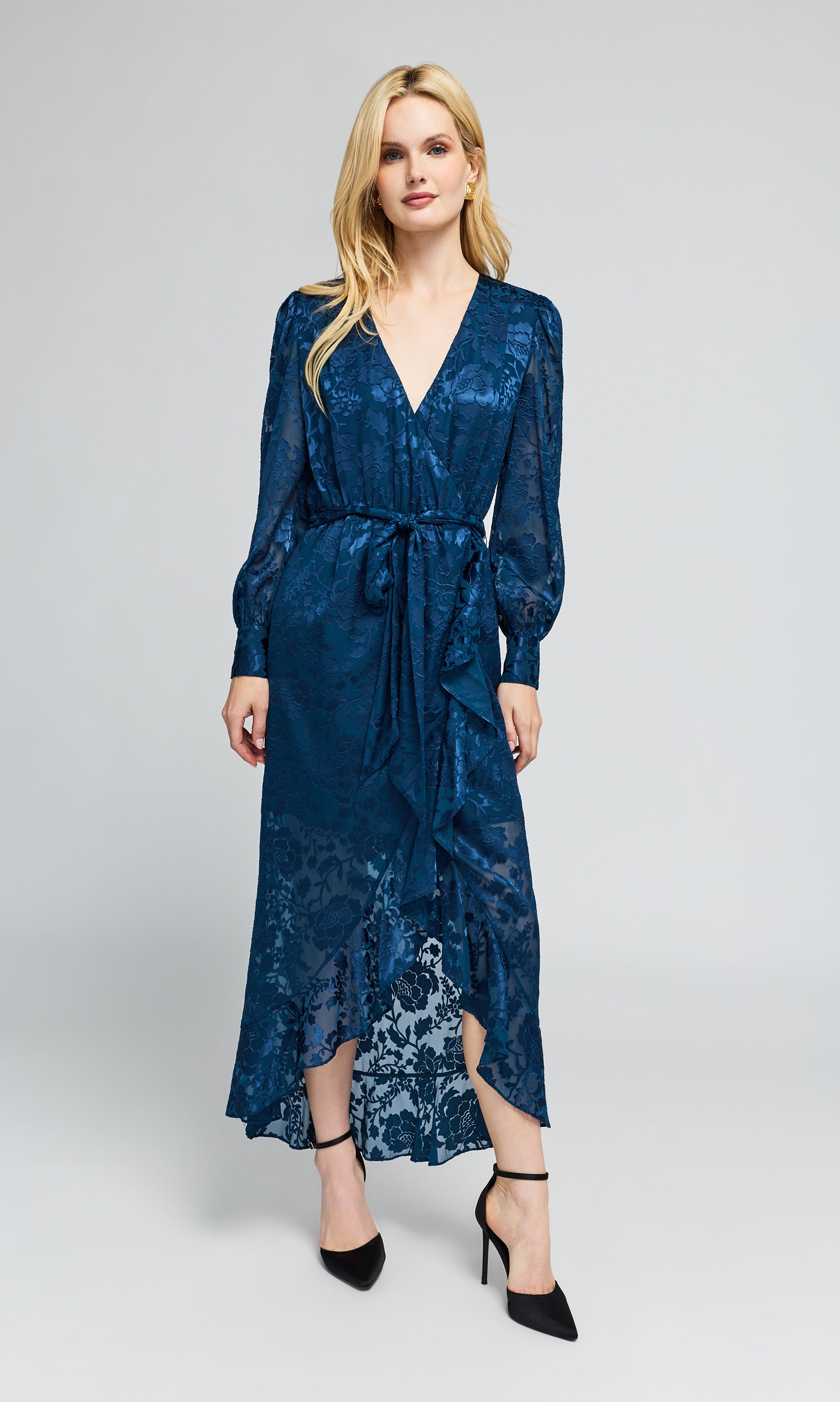 Model wearing a long-sleeved wrap midi dress in a deep blue jacquard pattern with a matching tie belt.