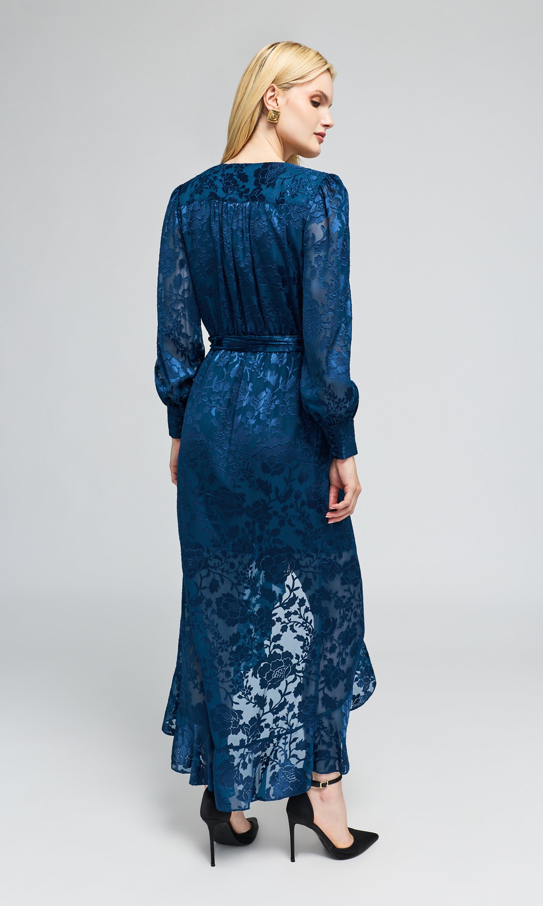 Back view of model wearing a long-sleeved wrap midi dress in a deep blue jacquard pattern with a matching tie belt.