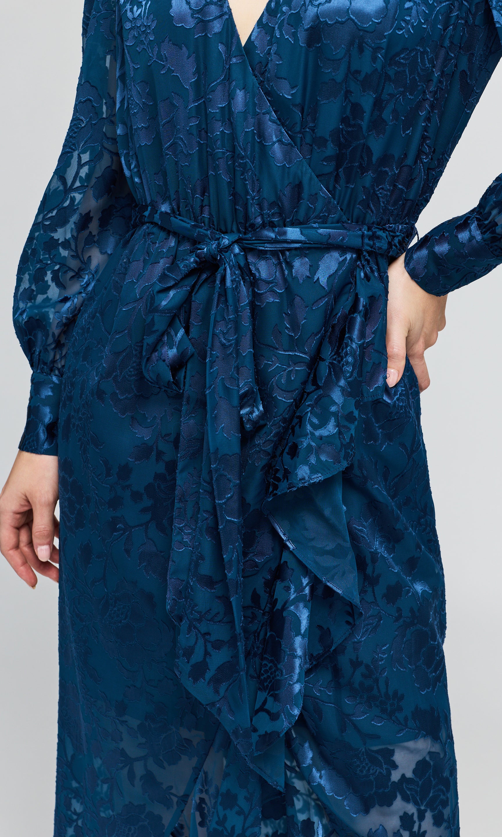 Close-up of a dark blue long-sleeve wrap dress with a matching waist tie and a subtle tonal floral jacquard pattern.